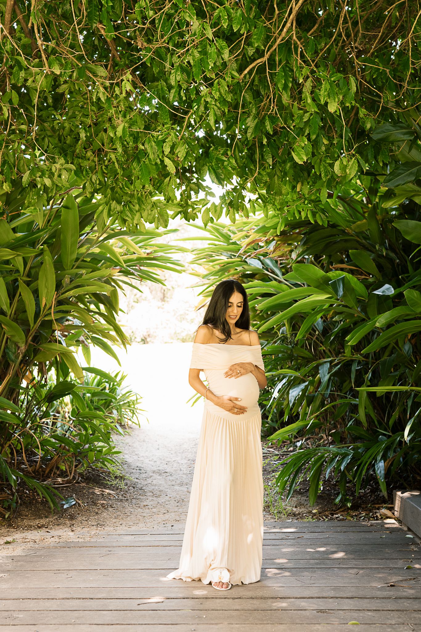 Maternity photoshoot in a tropical garden setting with soft natural lighting.