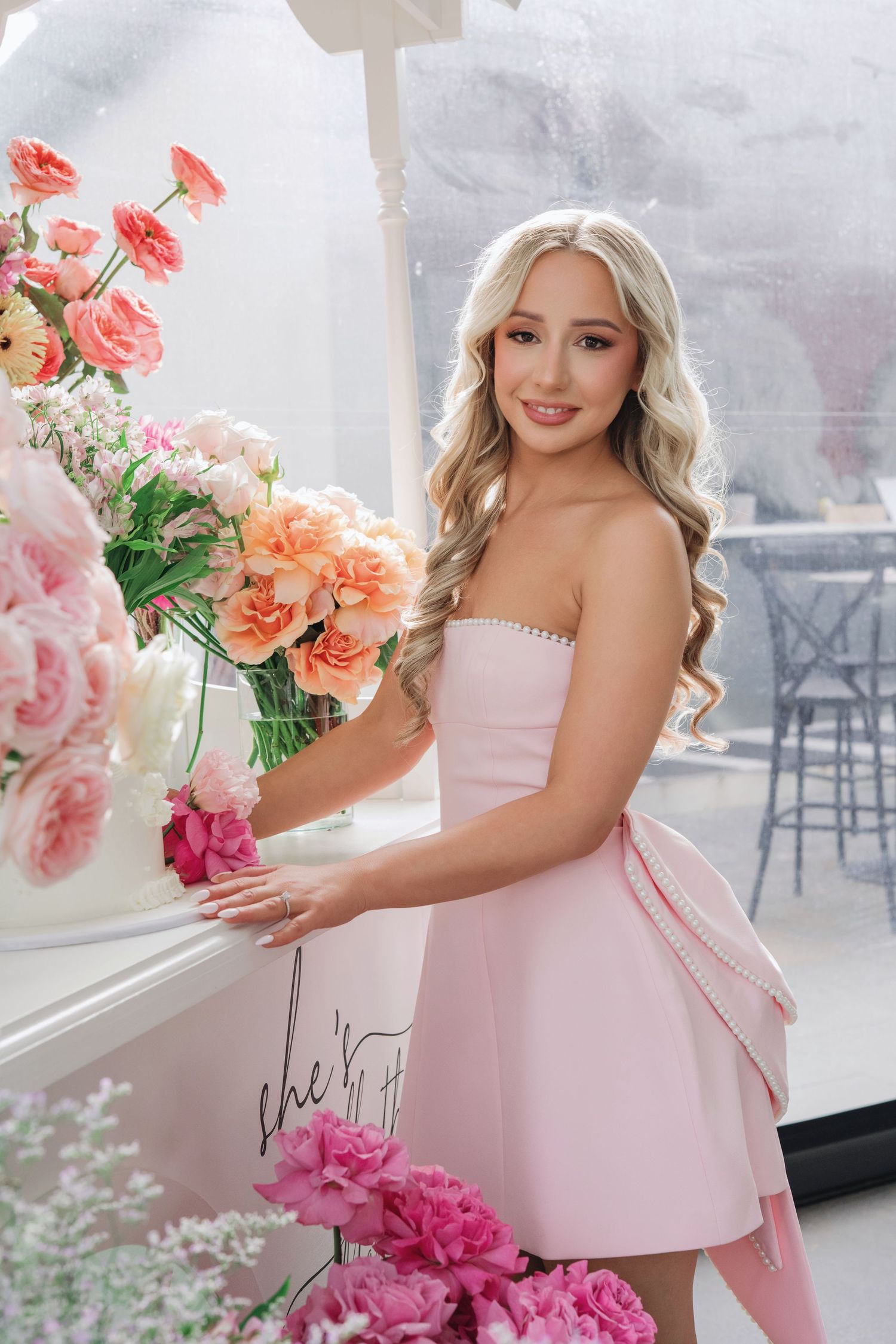 A dreamy spring scene with pink strapless dress and coral flowers arranged by a window in soft natural light.