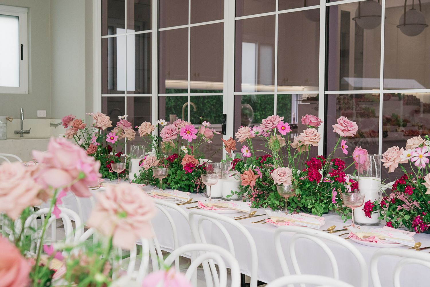 Wedding reception table with pink and white flowers running down the center and white chairs.