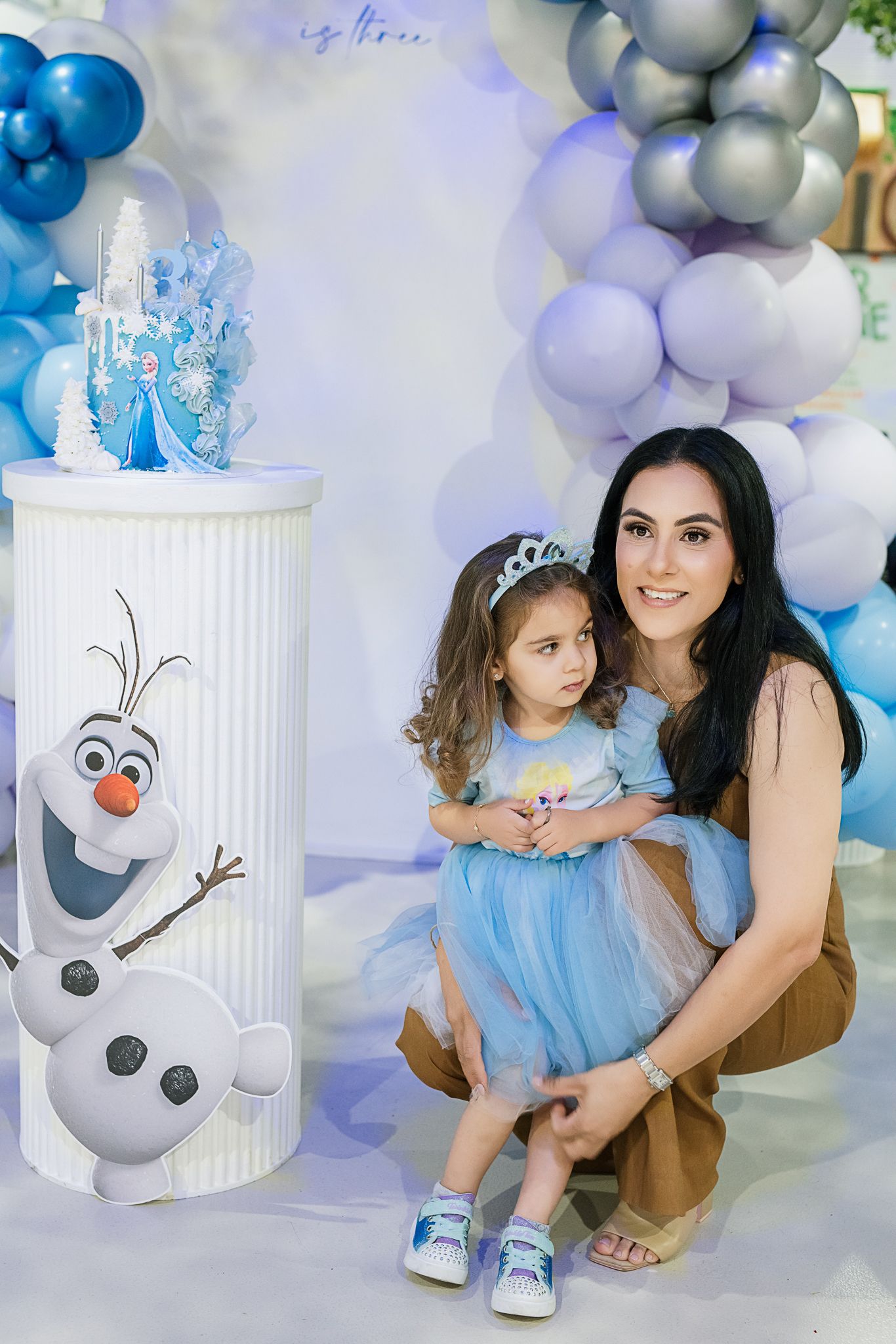 Blue and white balloon arch decorates party scene with Olaf-themed cake display.