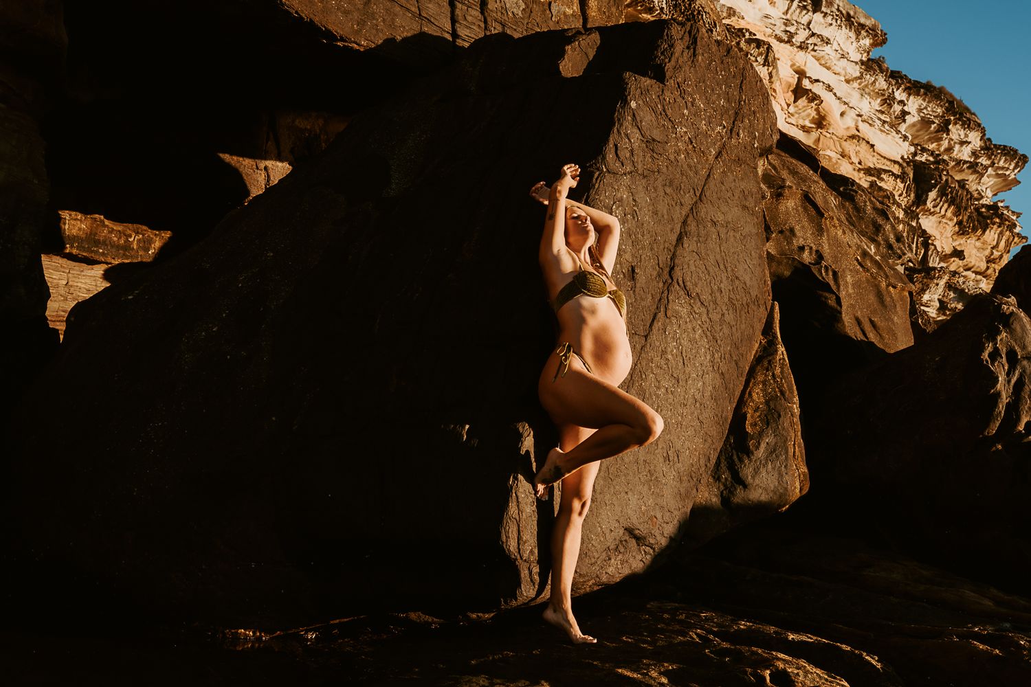 Artistic nude silhouette against textured rock formations in natural lighting.