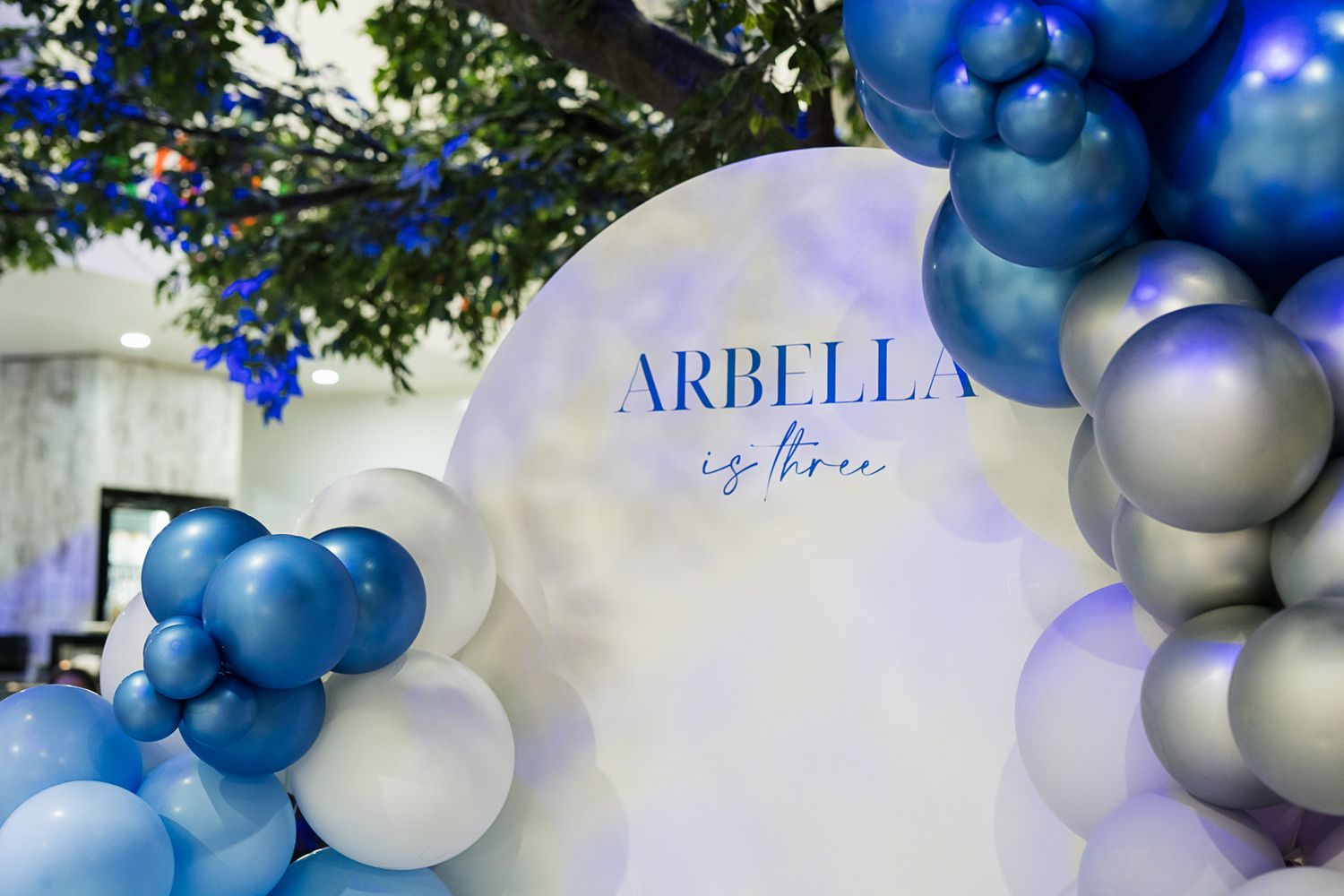 Blue and silver balloon arch with 'ARBELLA' text against a white backdrop.
