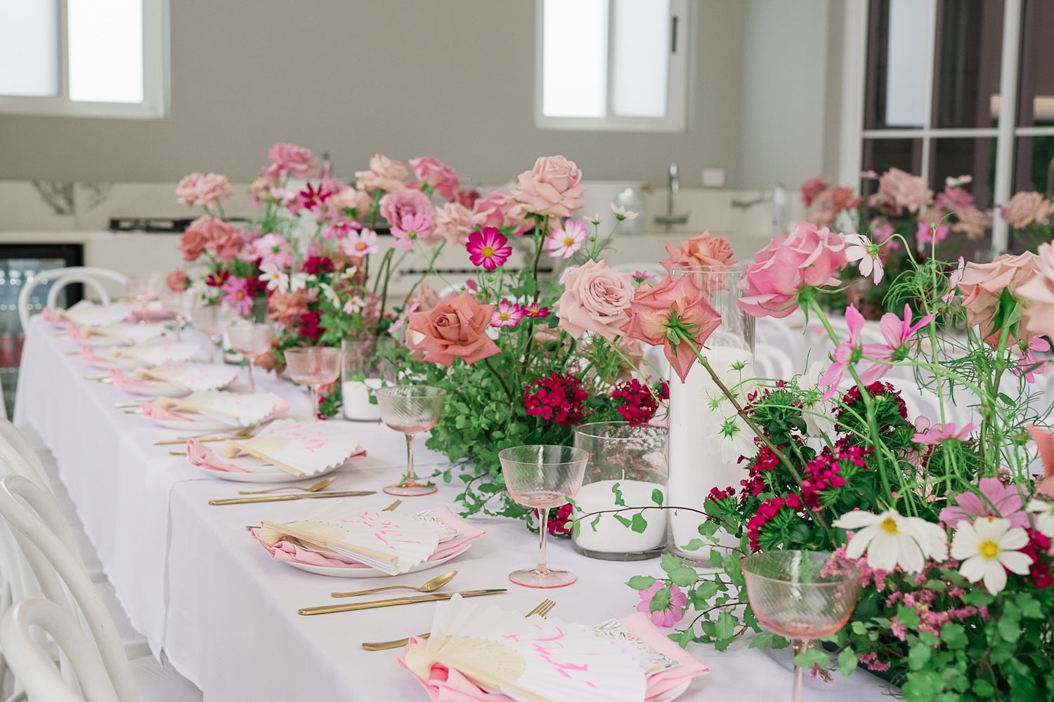 Long white dining table decorated with pink floral centerpieces and place settings for an elegant event.