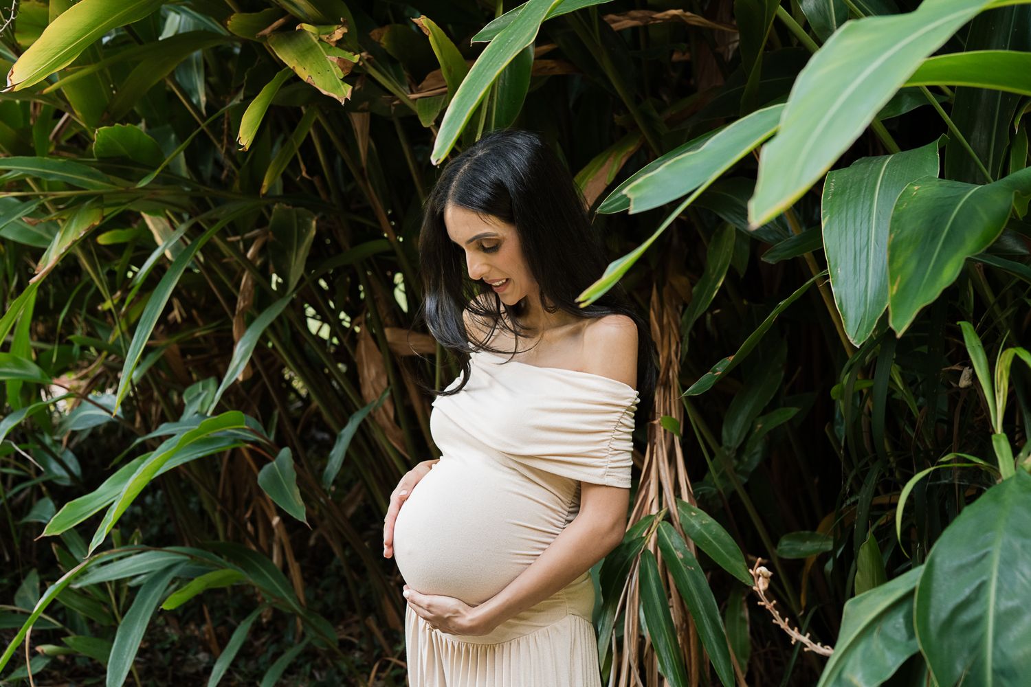 Artistic maternity photograph captured in a lush tropical garden setting.