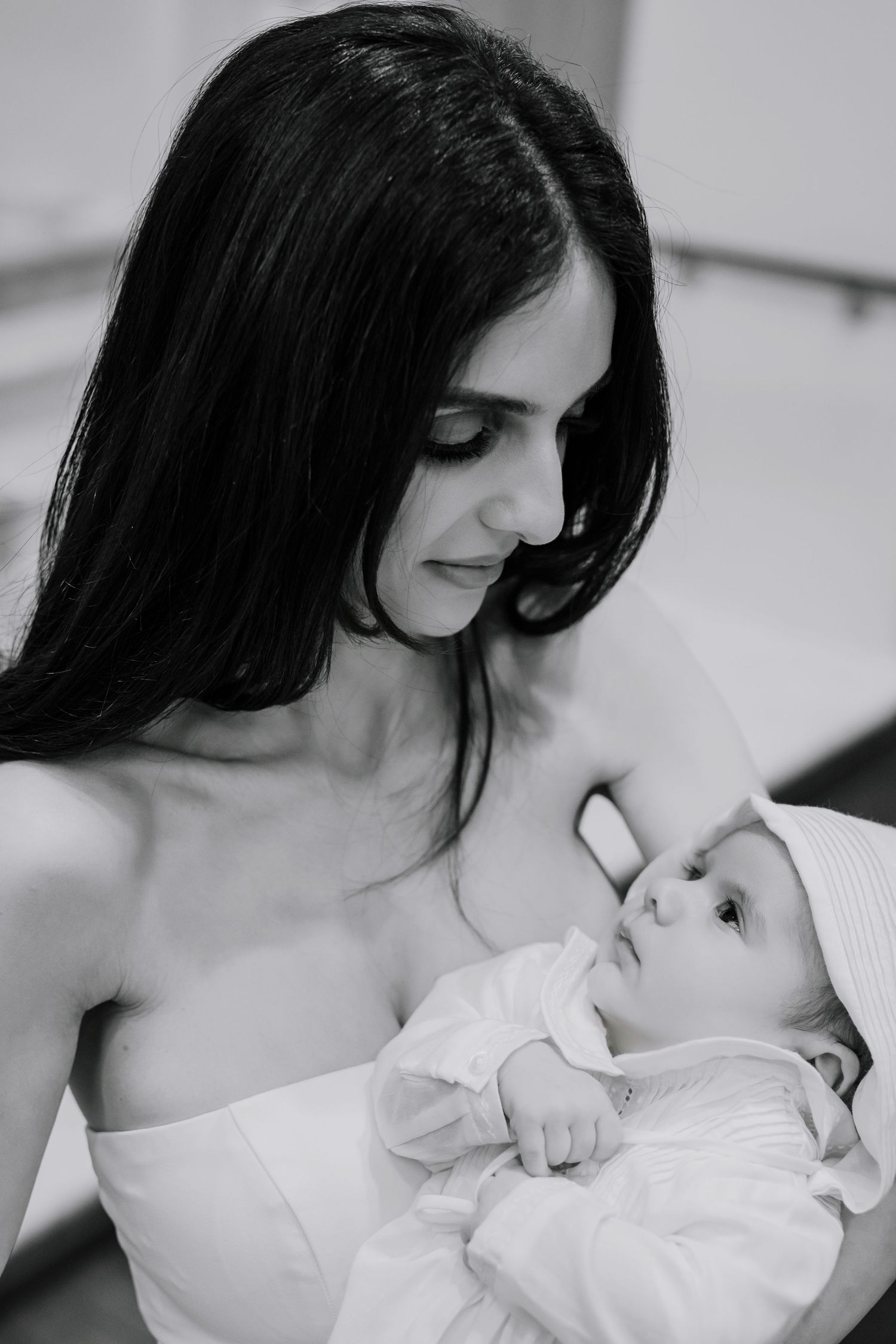 Tender moment between parent and newborn baby in white baptismal setting.