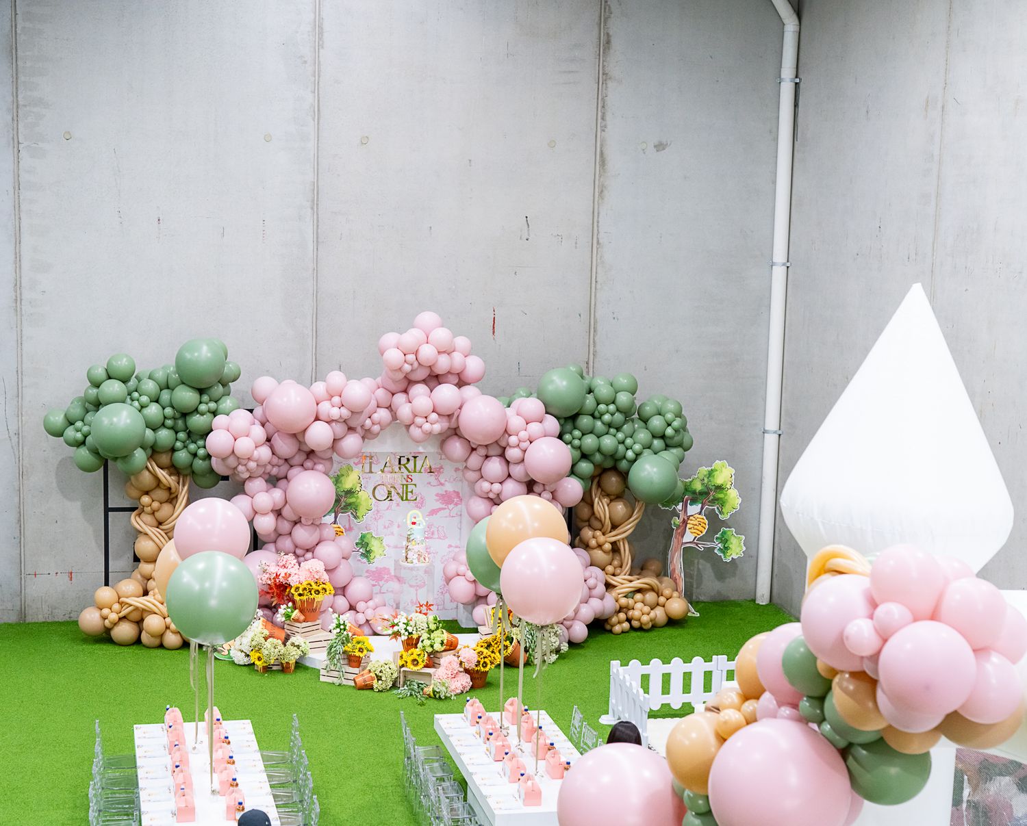 Outdoor party setup with pink and green balloon arch, floral decorations, and white furniture.