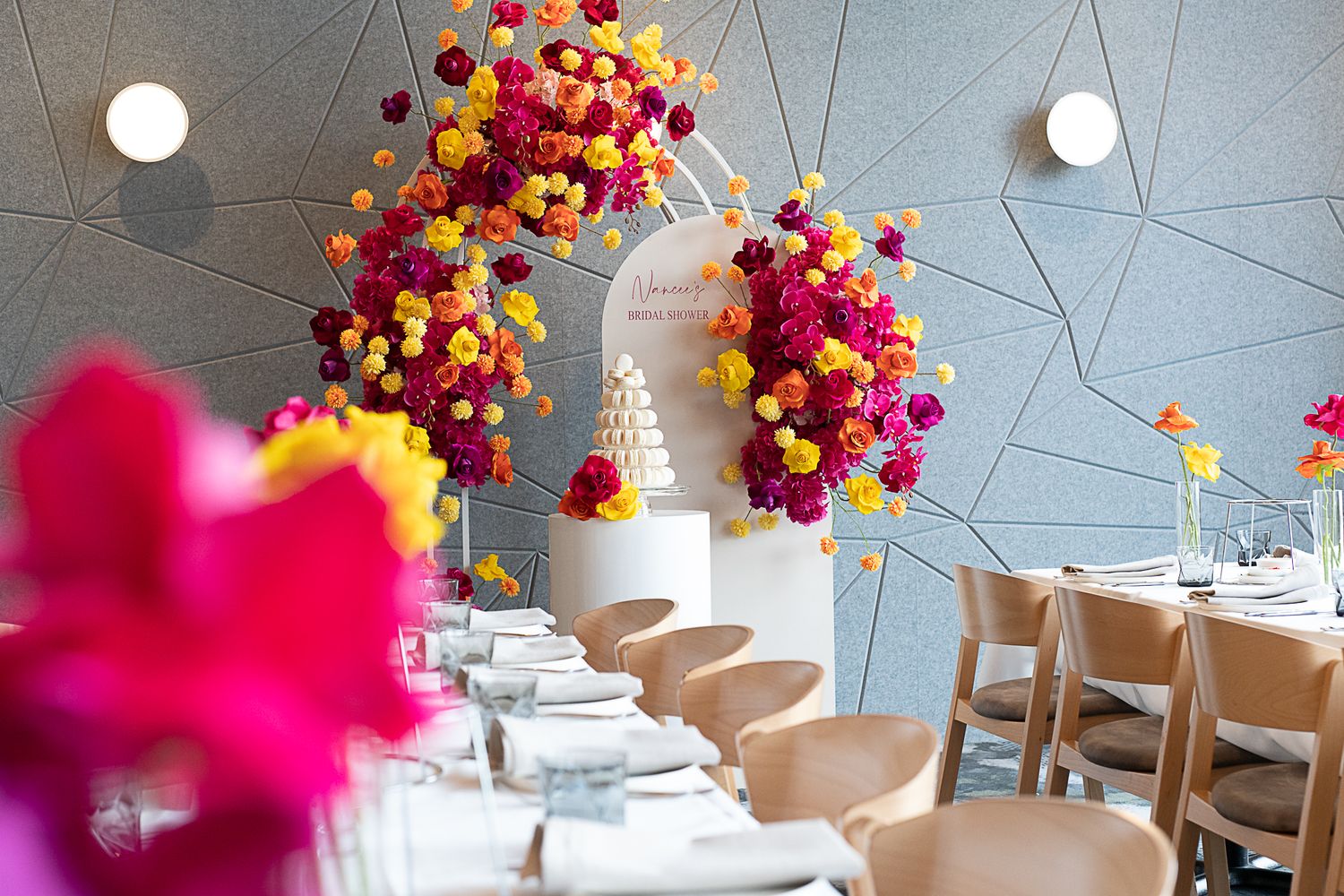 Vibrant floral and balloon arch installation over dining tables at event.