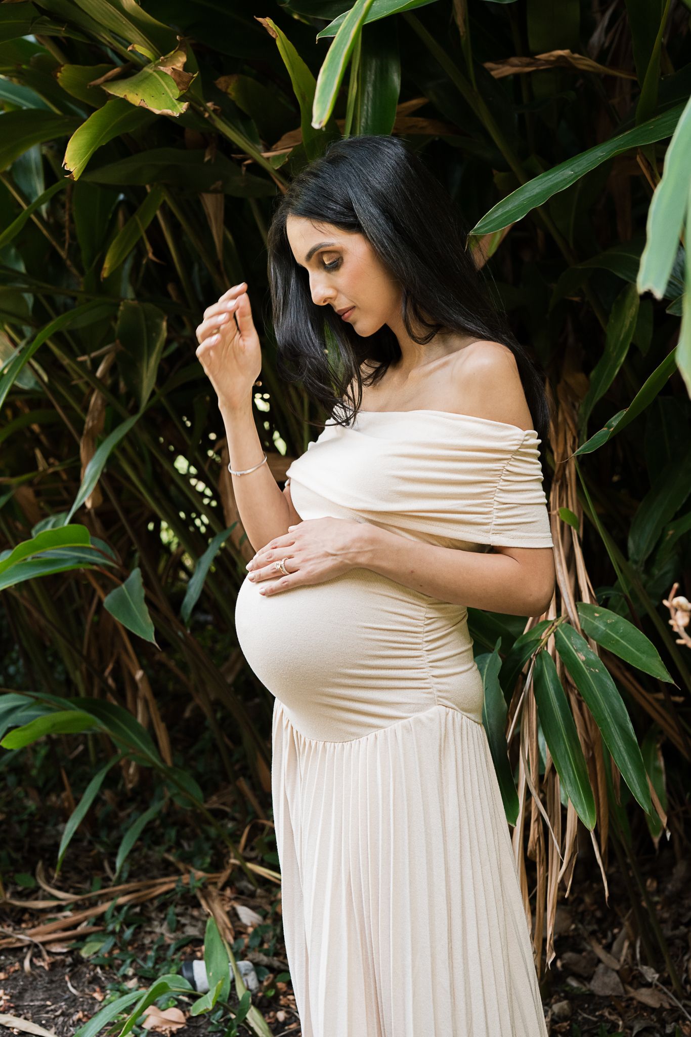 Intimate maternity portrait among tropical greenery with off-shoulder cream dress.