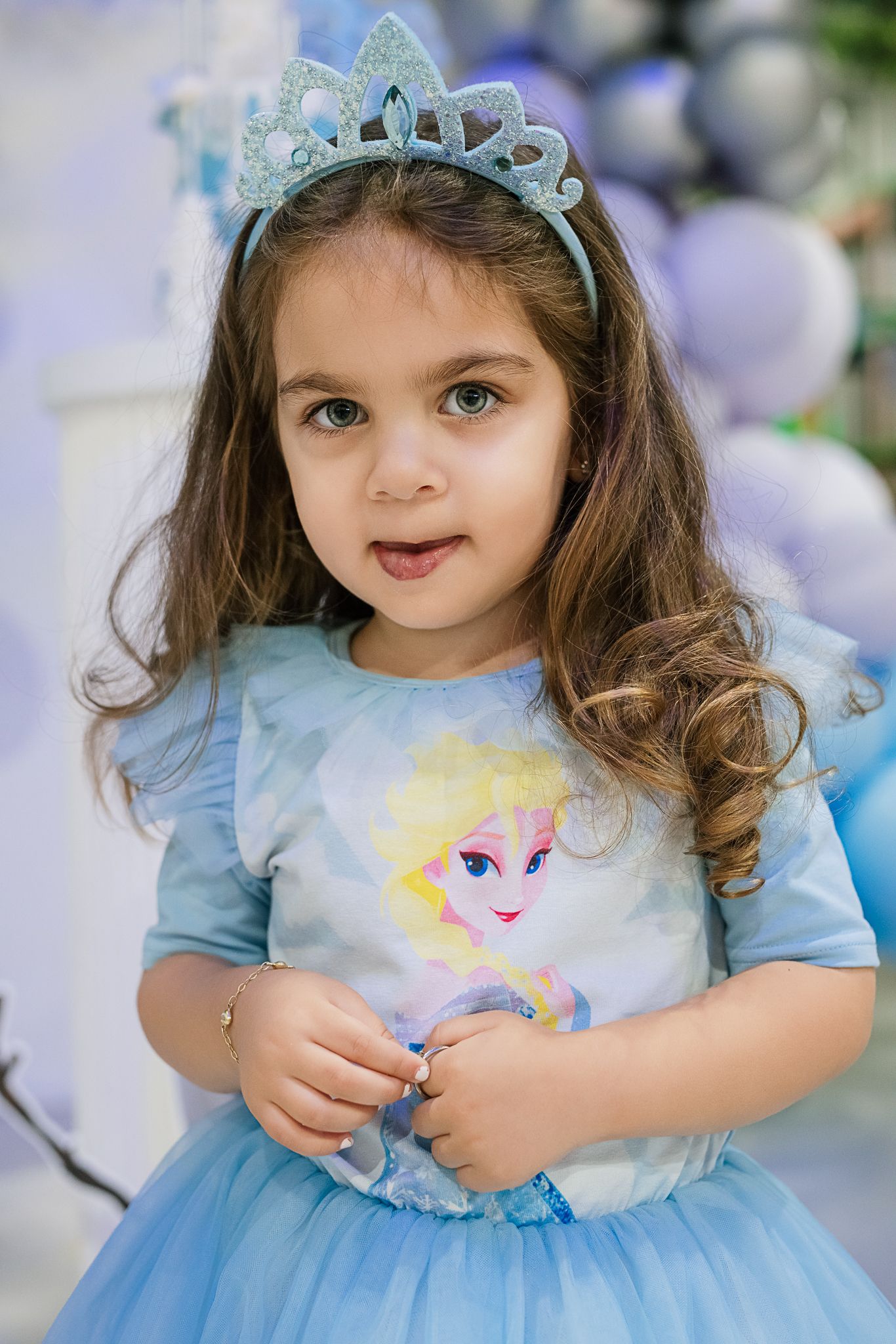Young child in a sparkly blue princess dress and tiara smiling at a themed birthday party.