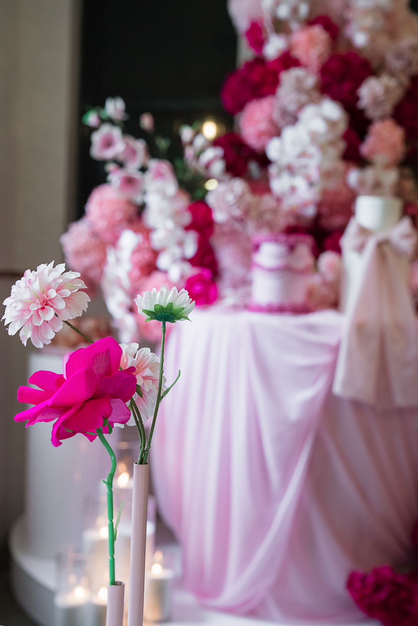 Pink and fuchsia flowers with white table draping and glowing candles creating a romantic atmosphere.
