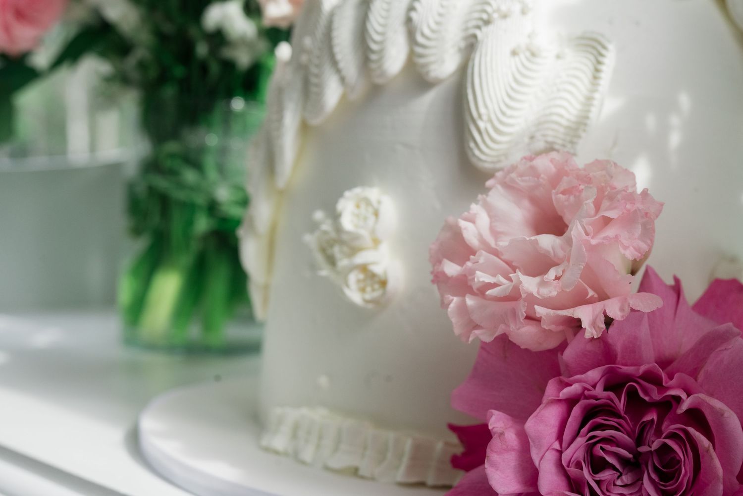 Close-up detail of a white wedding cake decorated with meringue swirls and pink rose flowers.