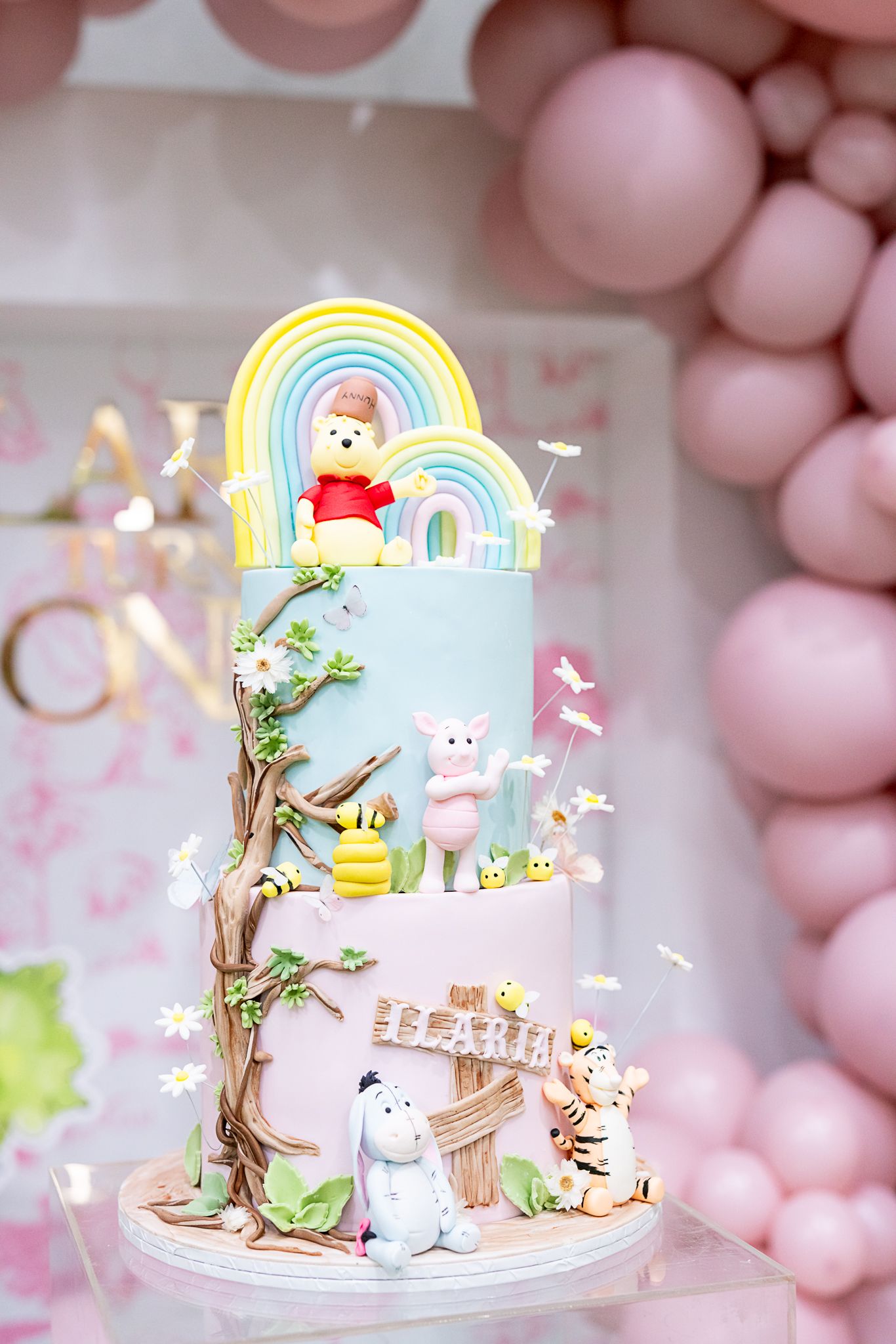 Whimsical tiered cake with rainbow, teddy bears, and woodland creatures in pastel colors.
