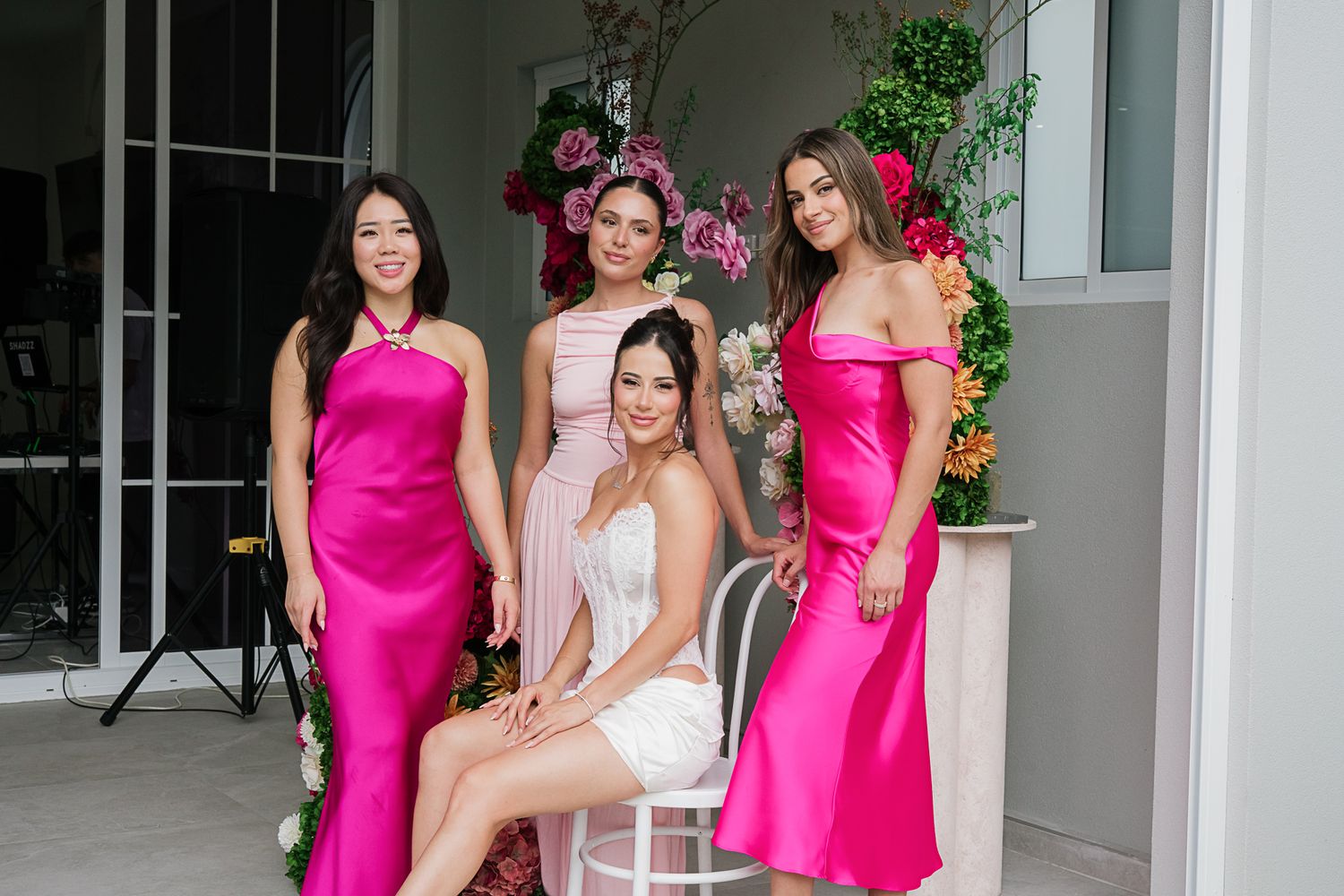Wedding party portrait featuring bright pink bridesmaid dresses and white bridal gown against floral backdrop.