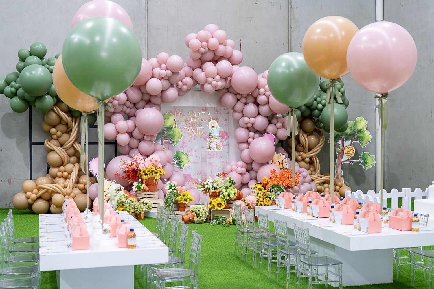 Elegant party space with balloon arch, floral centerpieces, and place settings arranged on artificial grass.