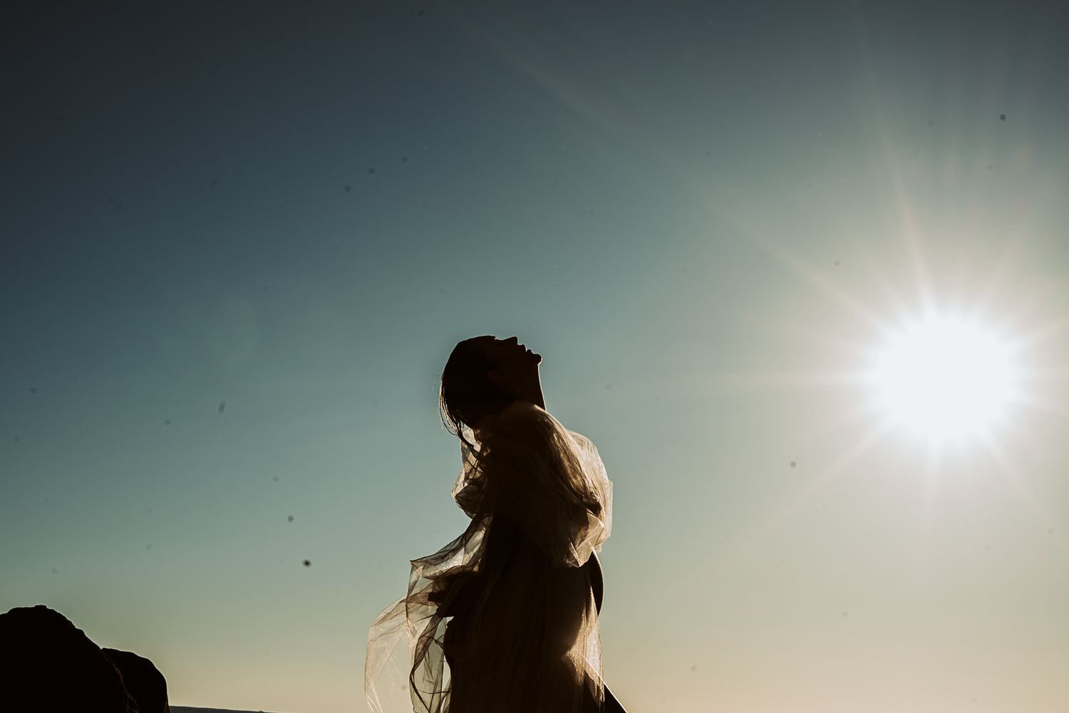 Backlit silhouette of person with long hair against bright sun and blue sky.