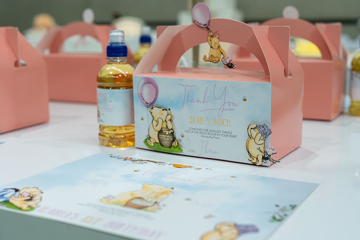Pink favor boxes with whimsical animal designs and matching party favors displayed on white table.