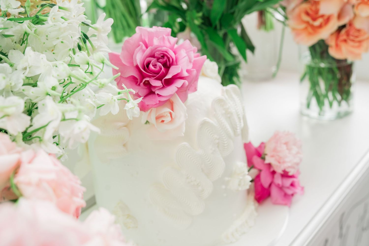 A delicate pink rose rests atop a frosted glass vase with soft floral arrangements in the background.