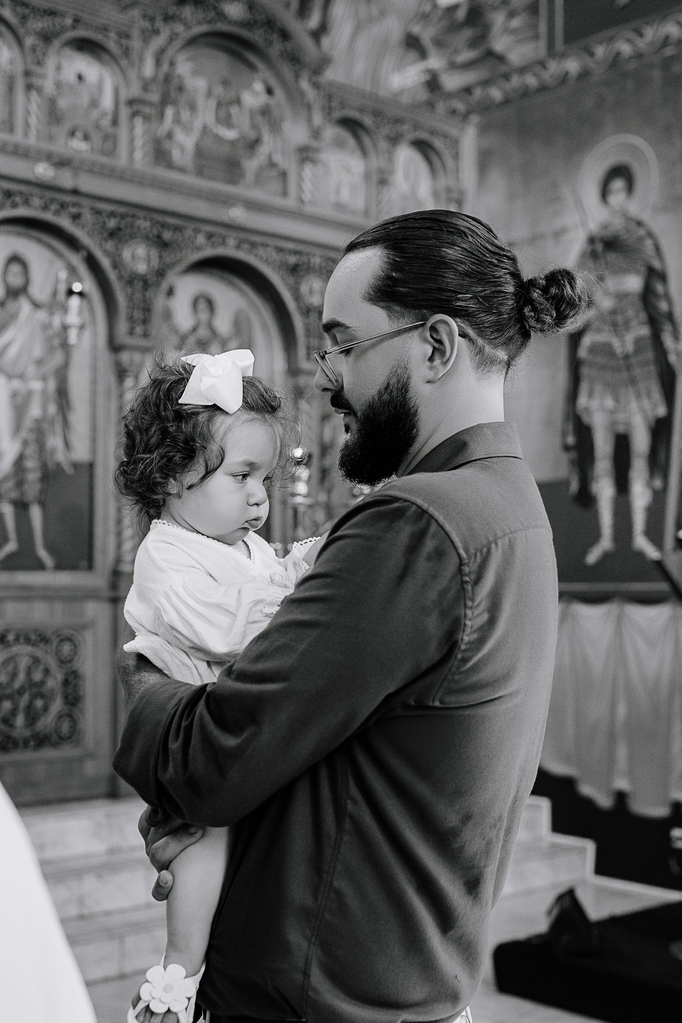 Parent holding child inside ornate church with religious icons on wall.