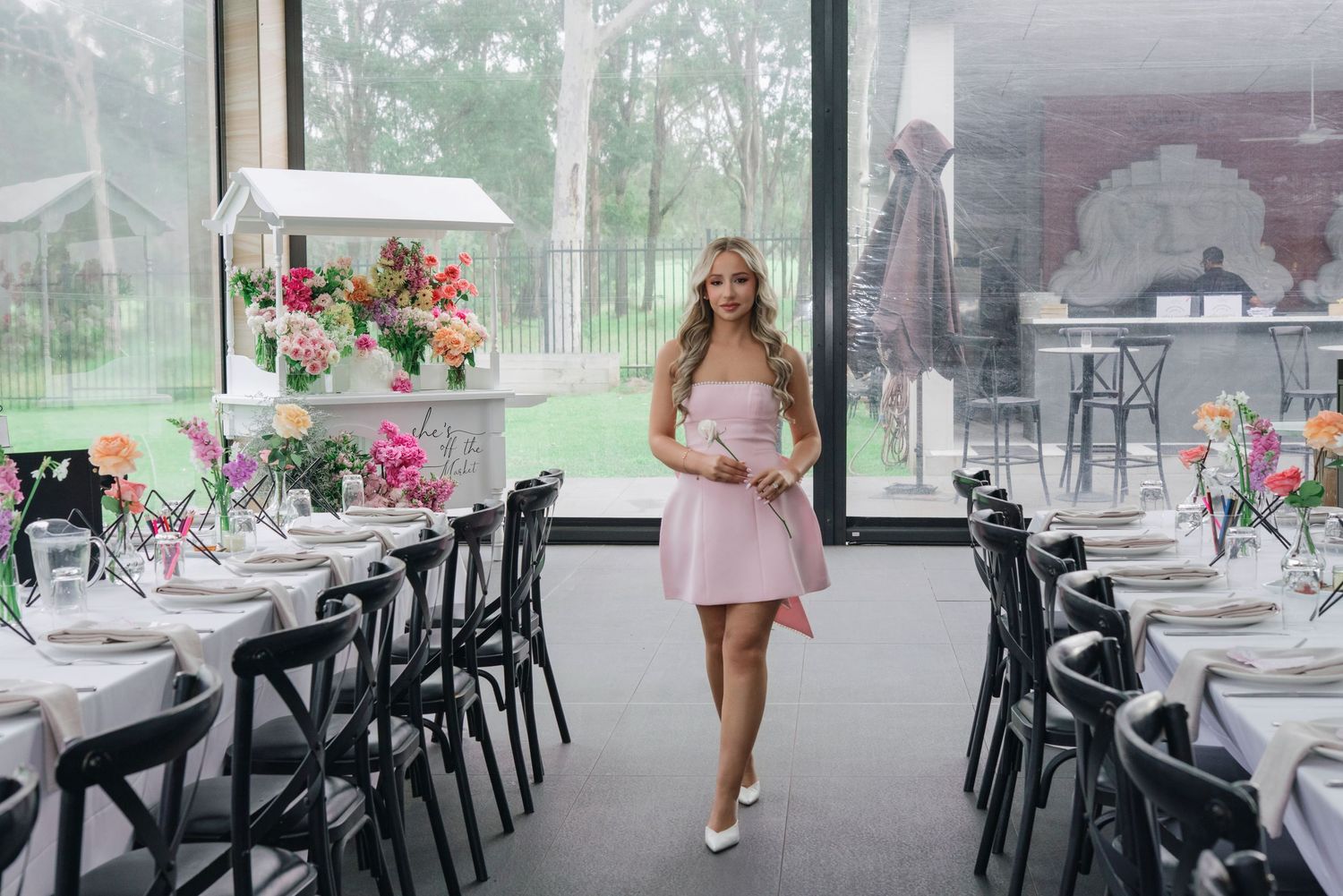 A pastel pink themed spring bridal shower setup with black chairs and floral centerpieces in an elegant glass-enclosed venue.