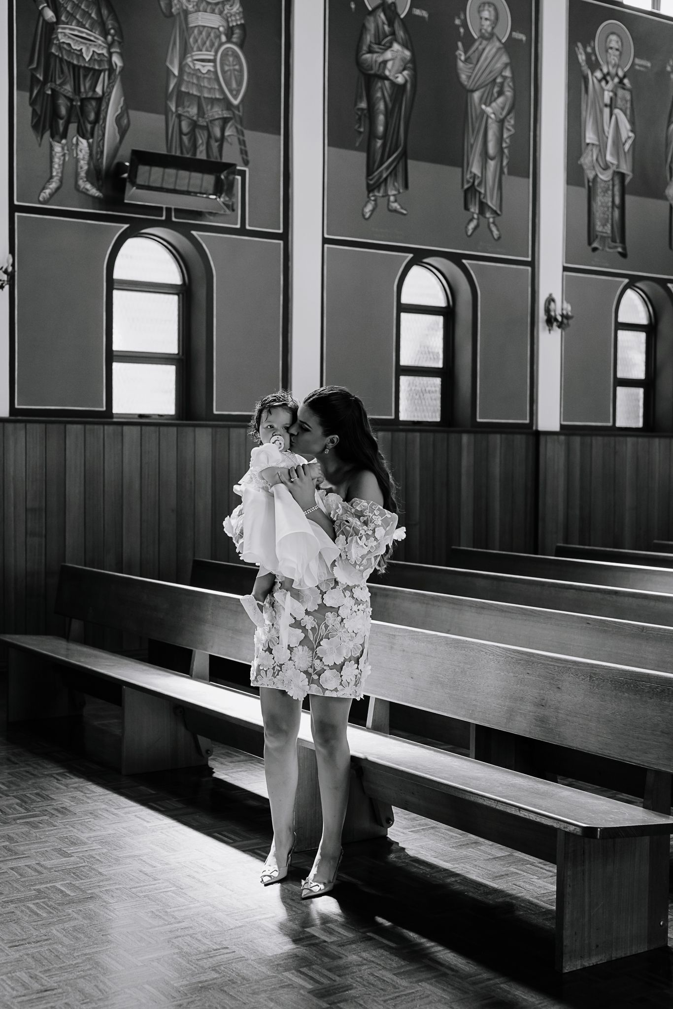 Parent and child sharing intimate moment in church pew with religious artwork on walls.