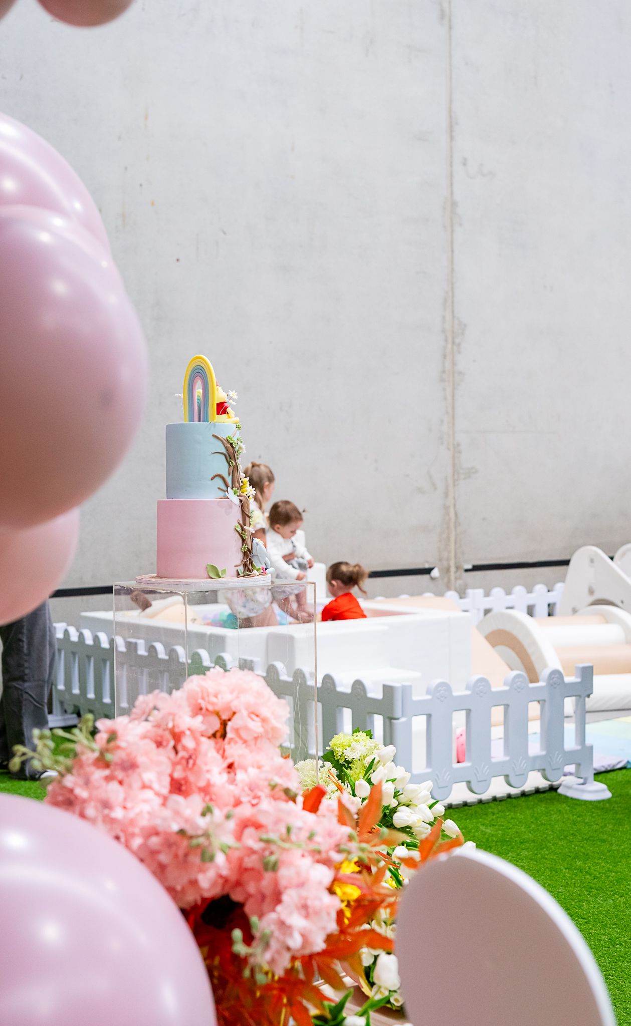 Pastel party setup with white picket fence, balloons, and decorative cake display.