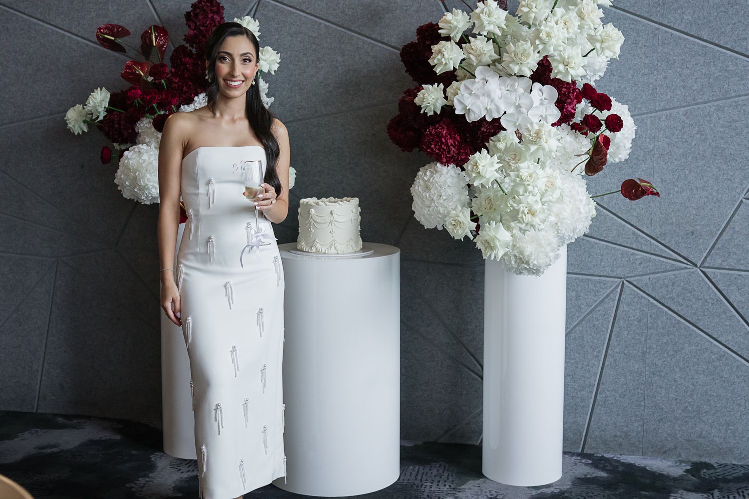 Elegant bridal scene with white cake and floral arrangements featuring red and white flowers.