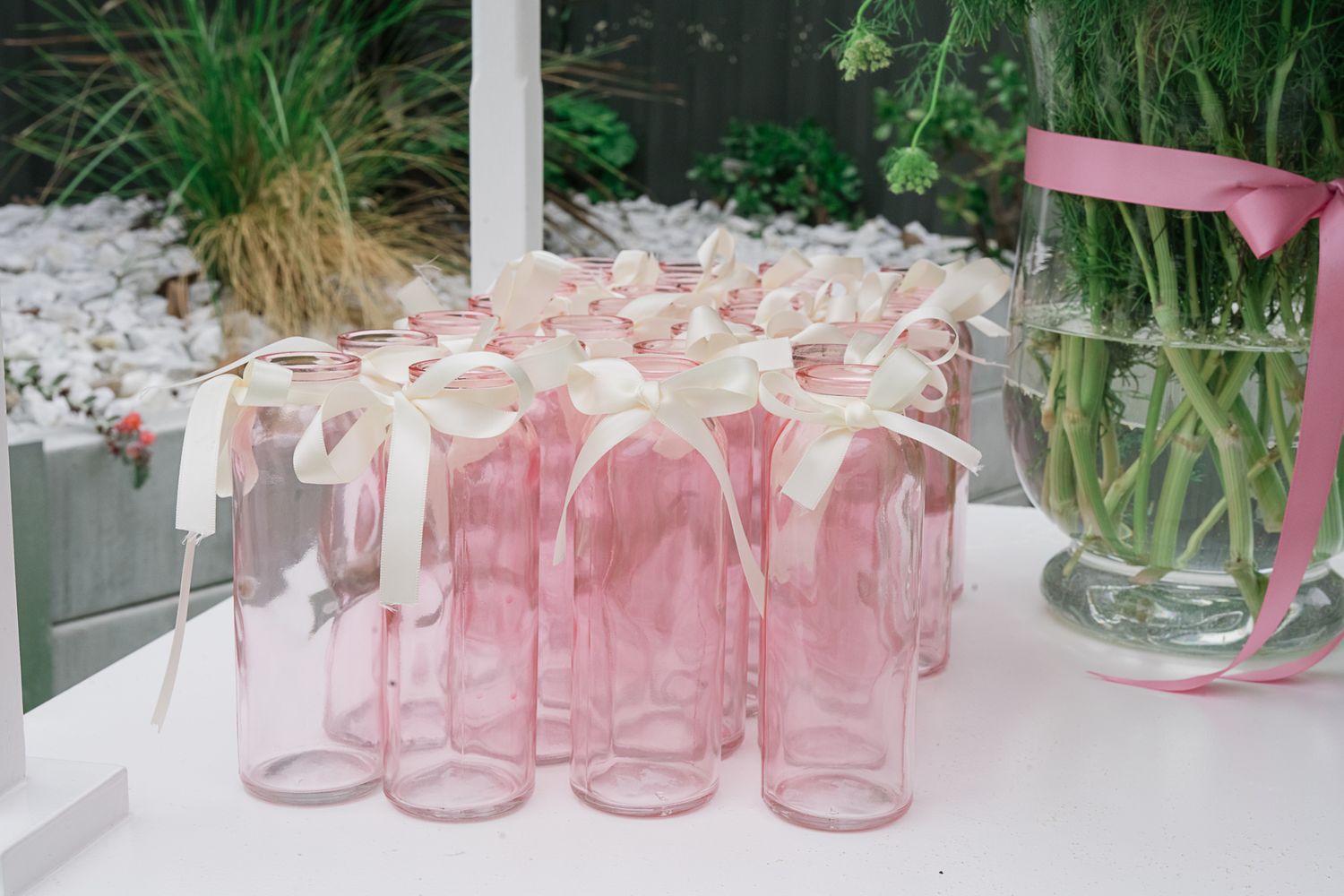 Row of pink glasses with white ribbon bows arranged on a white table.