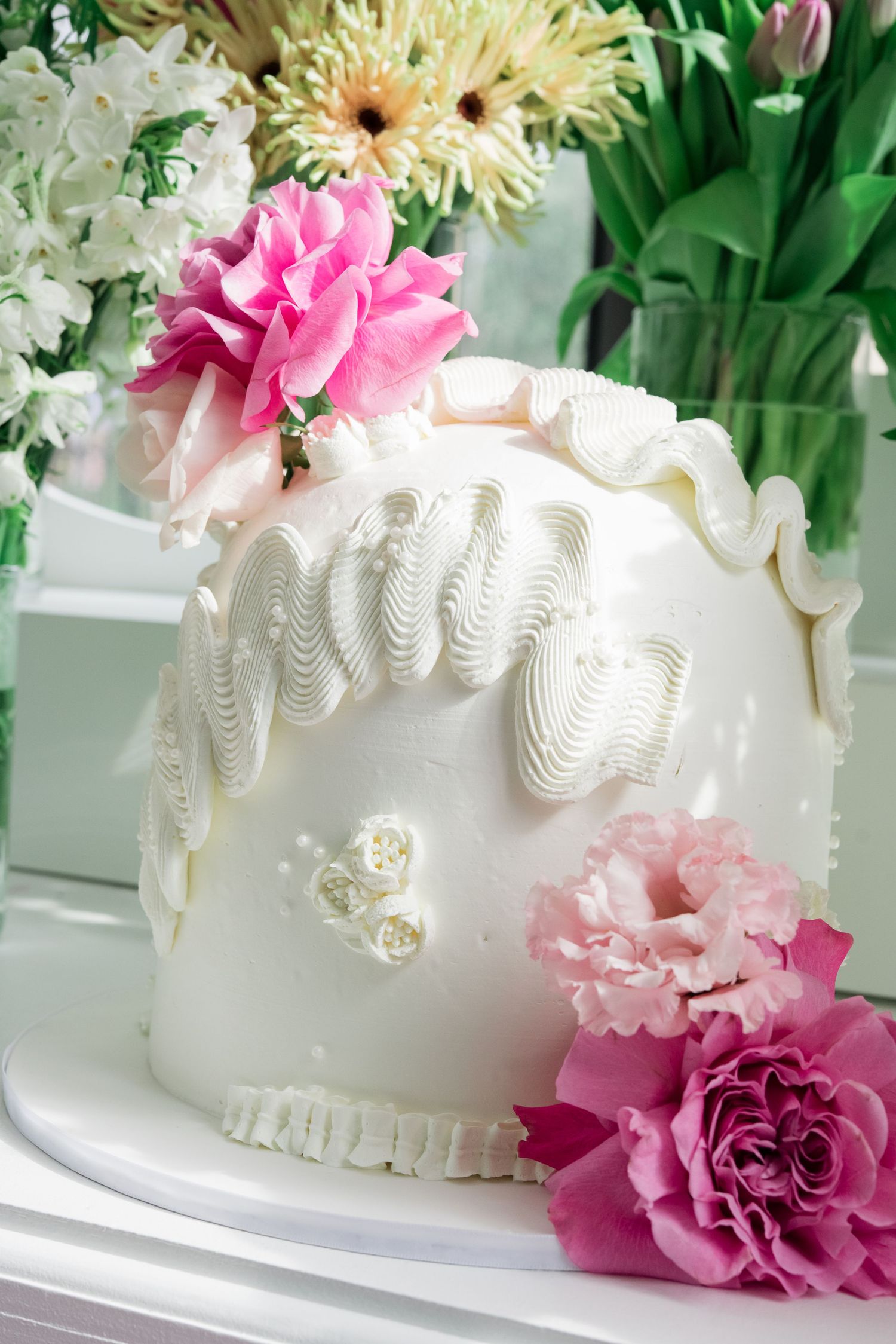 White wedding cake with elegant swirled icing design decorated with pink and peach flowers and floral accents.