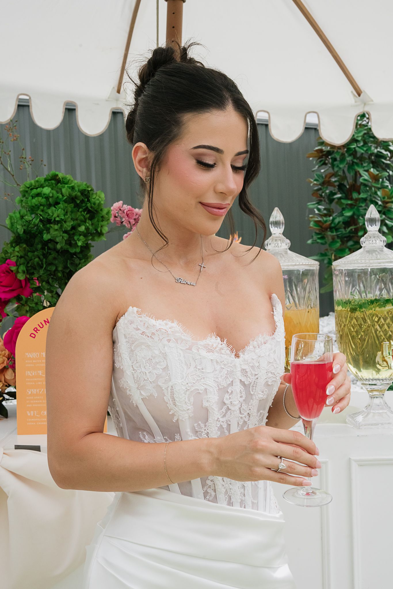 Elegant bridal portrait featuring white lace dress and champagne flute under outdoor canopy.