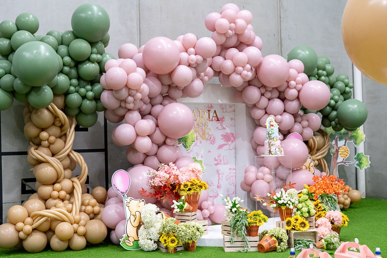 Whimsical party backdrop with pink and green balloon arch, floral arrangements, and party decorations.