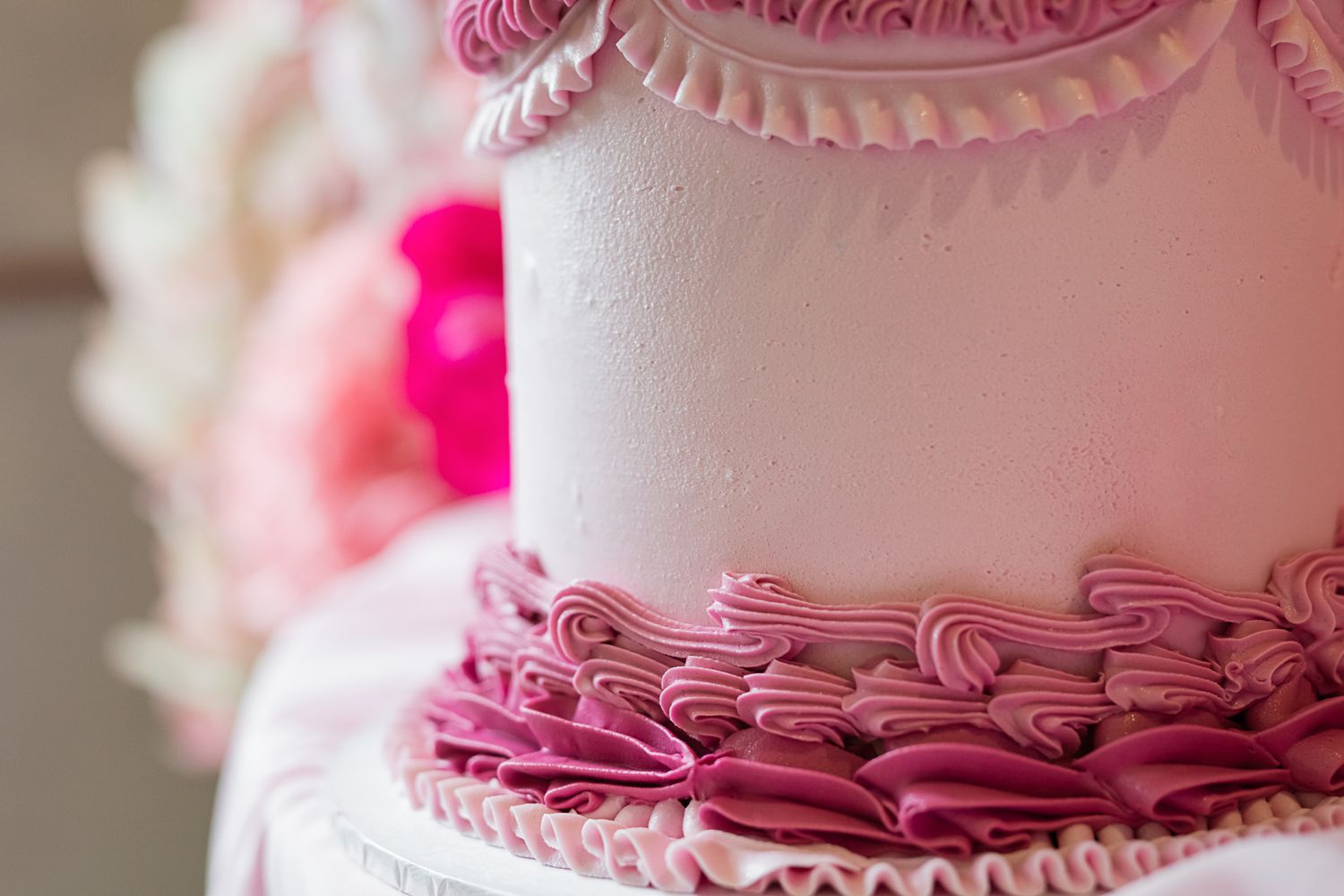 Close-up detail of pink ruffle piping decoration on a white wedding cake tier.