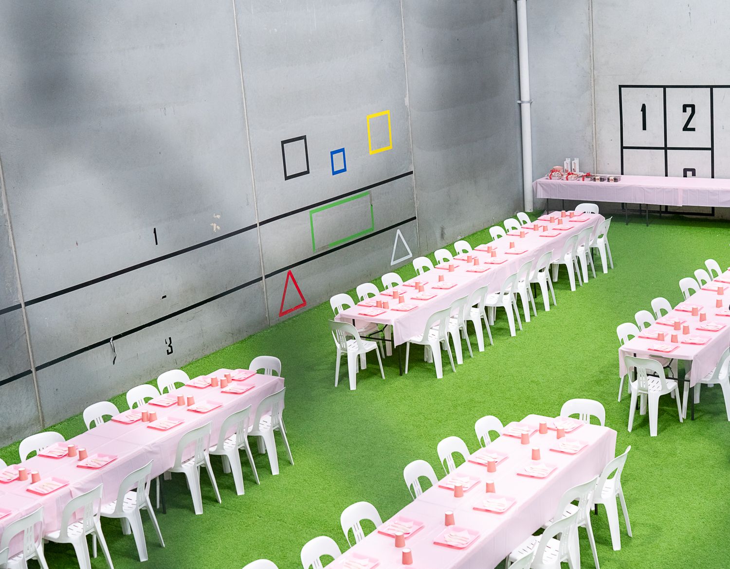 Clean party venue setup with rows of white chairs and pink table settings on artificial grass.