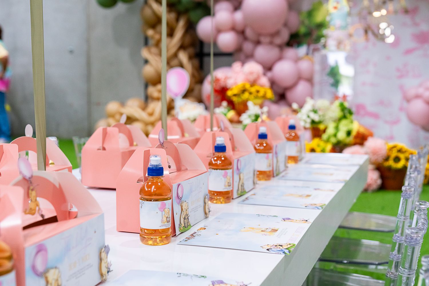 Pink party favors and drinks arranged in a row on an elegant table setting with floral decorations.