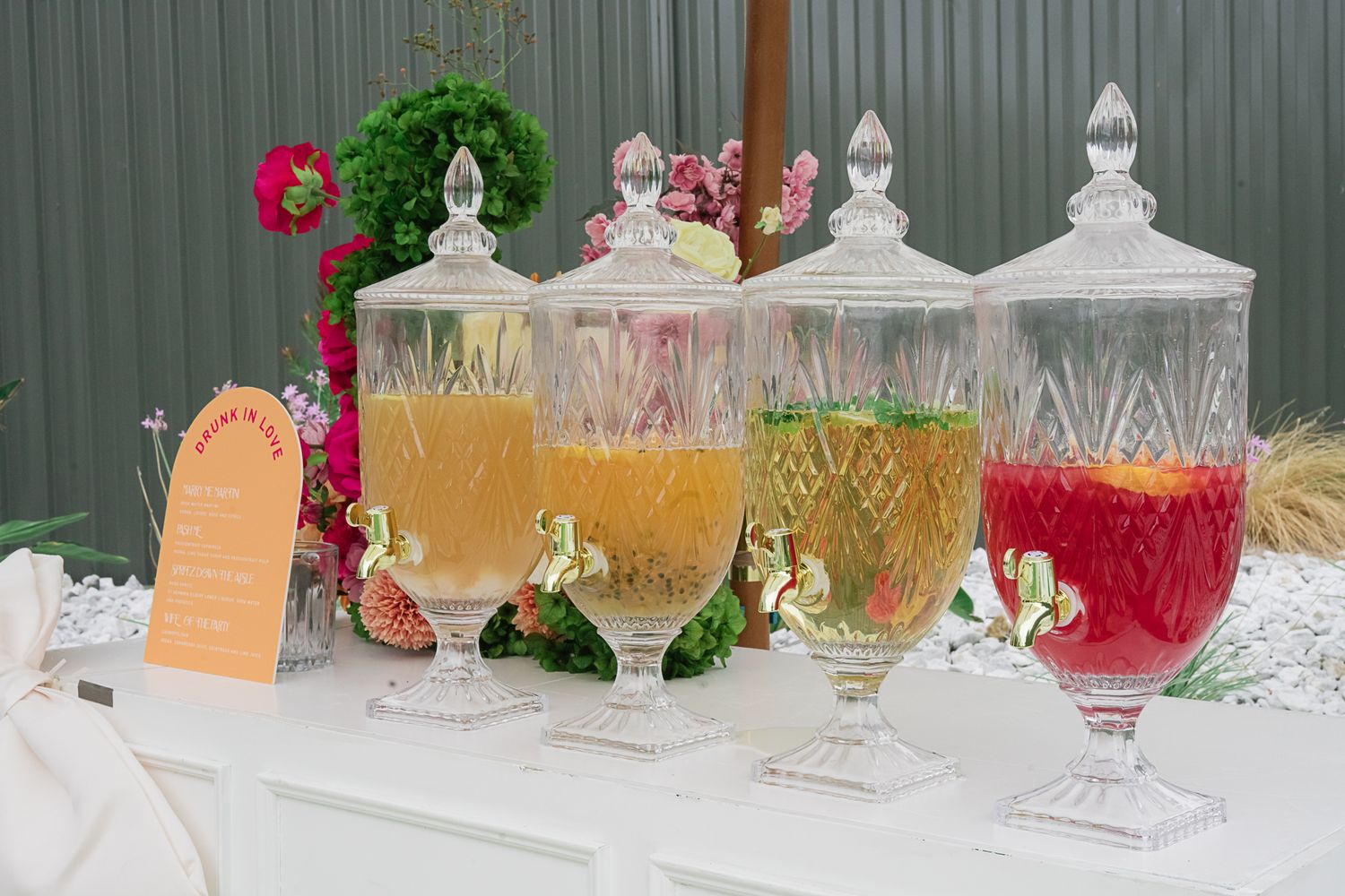 Vintage glass drink dispensers filled with colorful beverages and decorated with floral accents.
