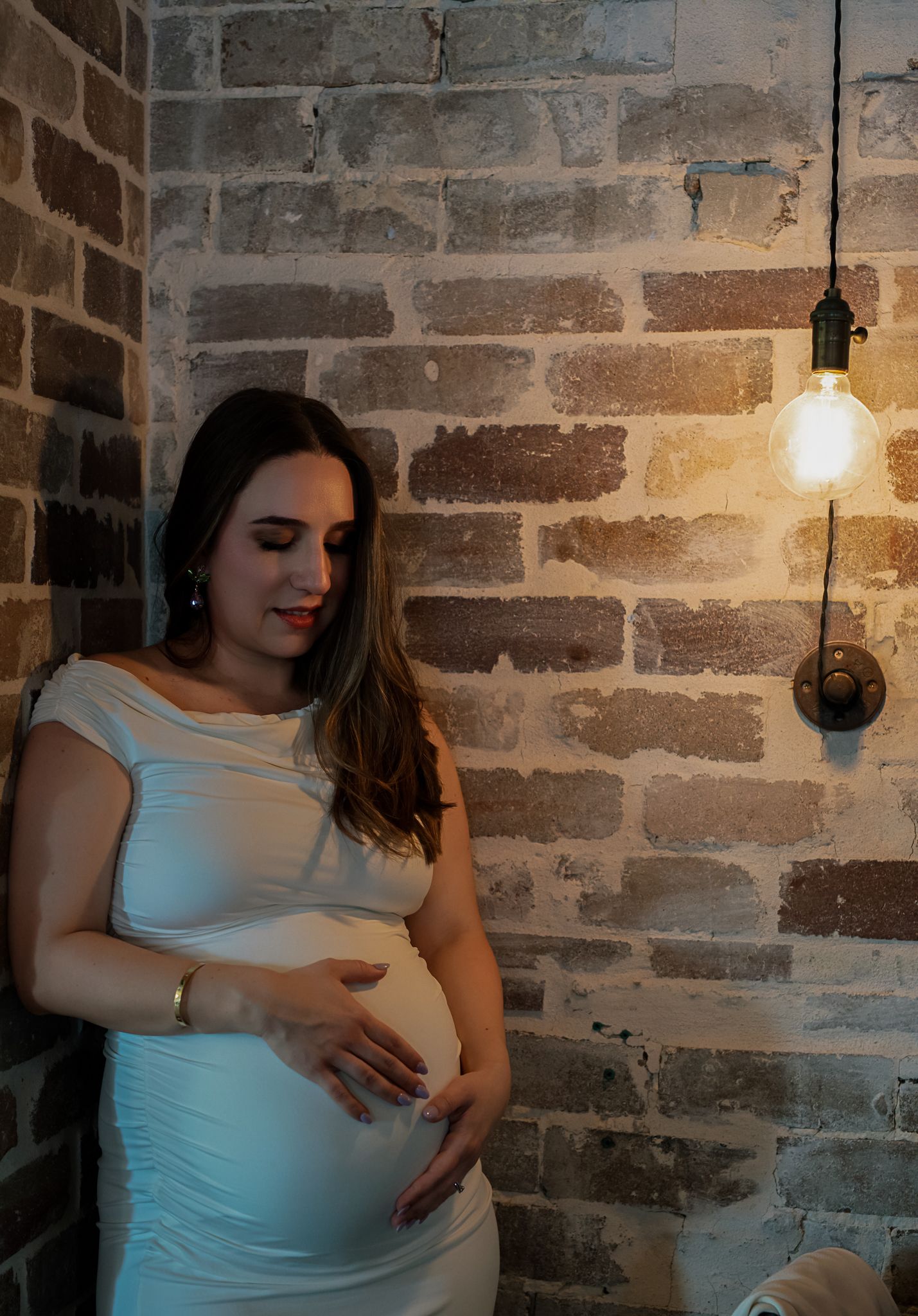 Maternity portrait with dramatic lighting against exposed brick wall and pendant light.