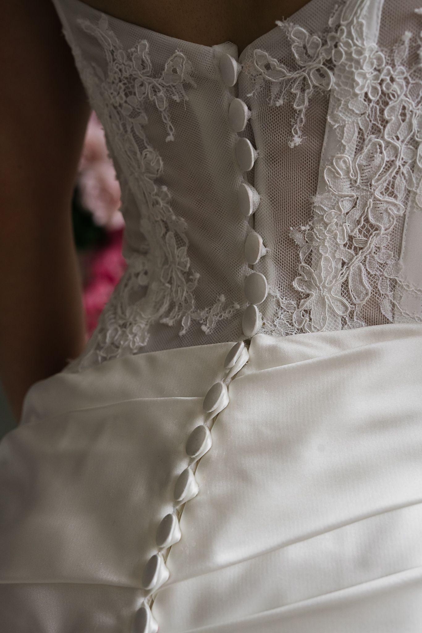 Detailed close-up of white wedding dress showing intricate lace pattern and button closure along the back.