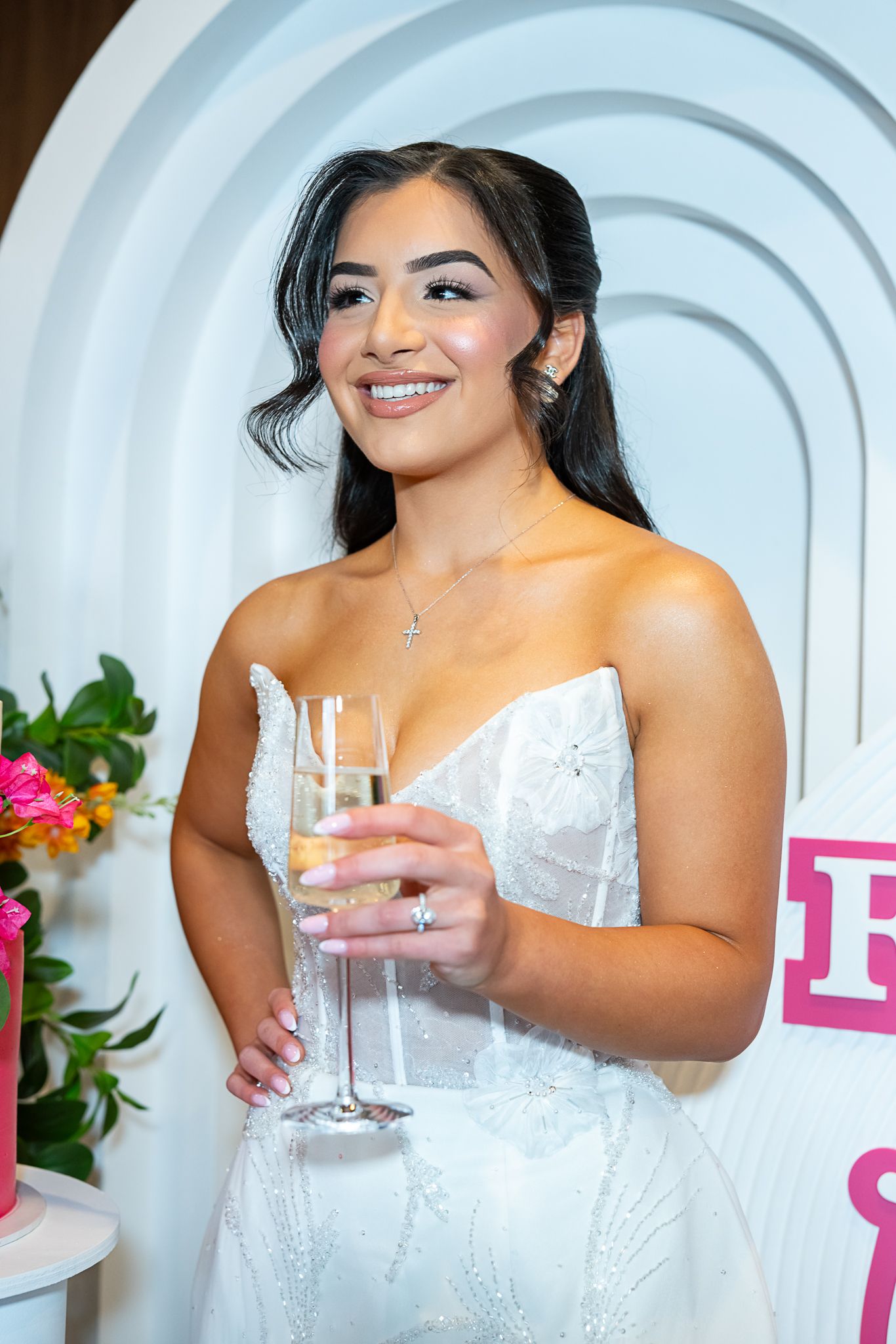 Wedding celebration setup with white arched backdrop, champagne glass and floral decorations.