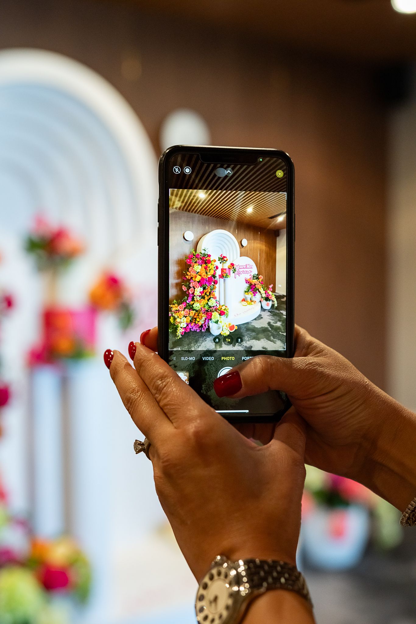Hands holding phone to capture photo of floral wedding backdrop with arch design.