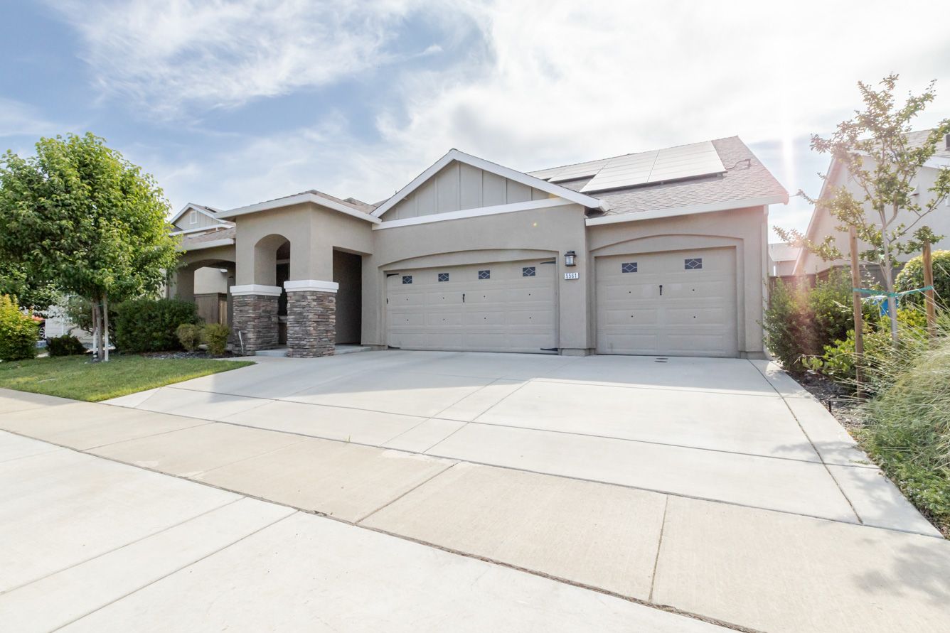 Modern single-story house with wide driveway and three-car garage featuring light gray exterior and white trim.