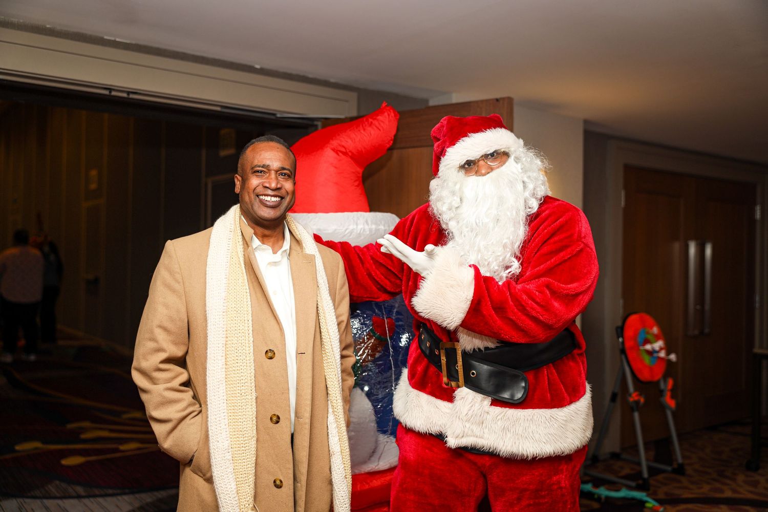 A person in a beige suit interacts with Santa Claus in a traditional red costume during what appears to be a holiday event.