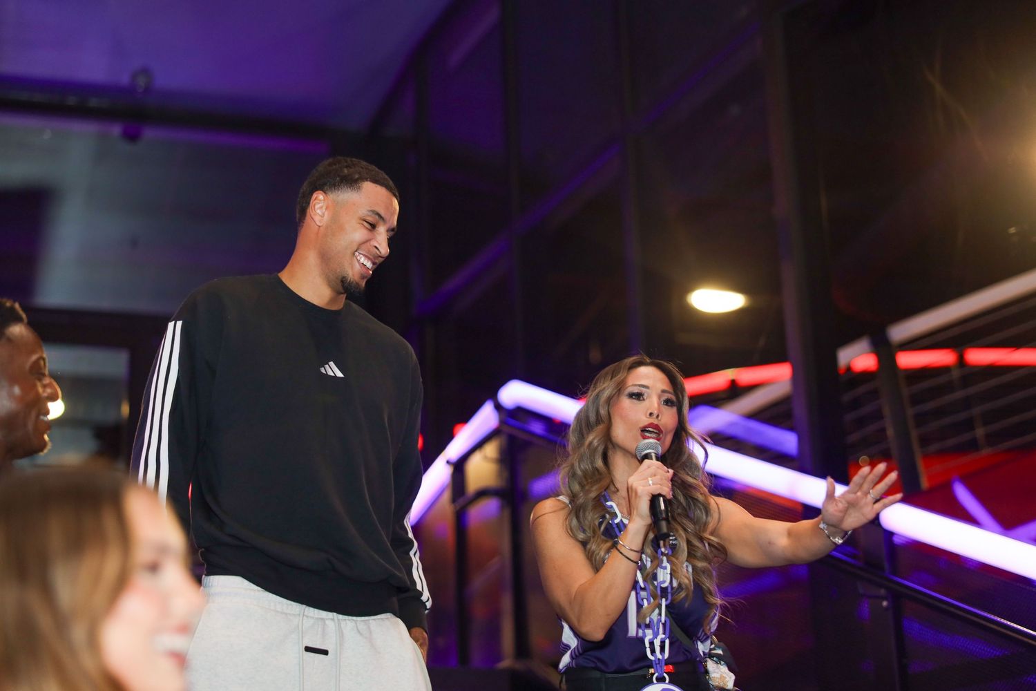 Performers on stage at a concert venue with purple lighting and dramatic spotlights creating an energetic atmosphere.