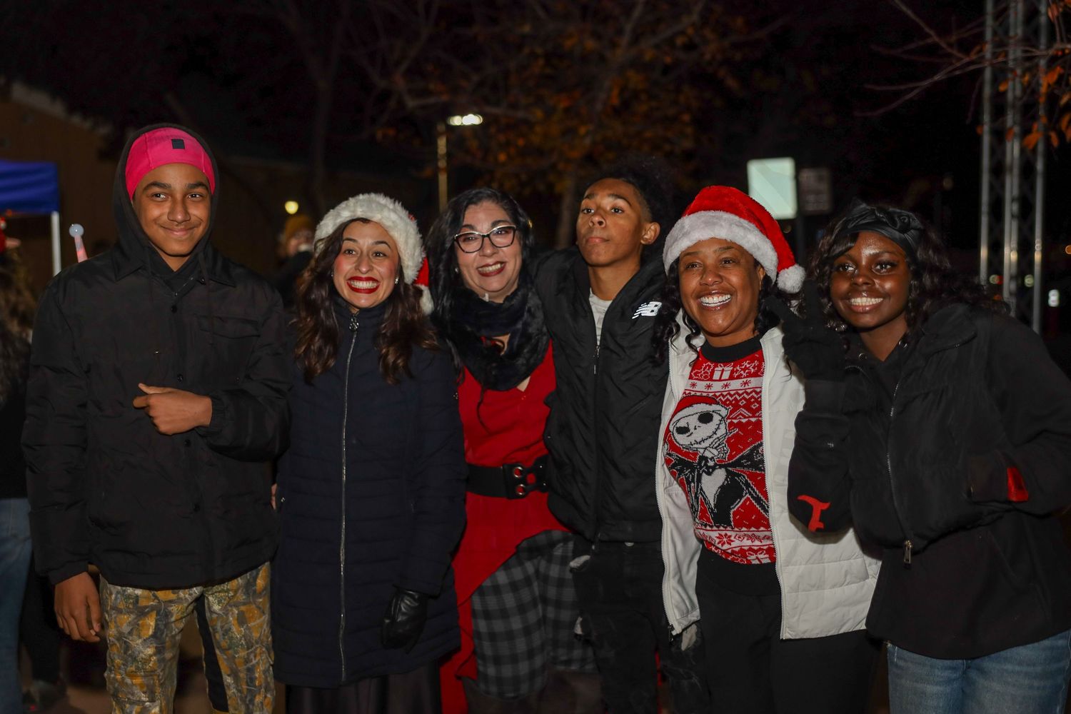 A group of people wearing winter hats and warm clothing stand together at night.