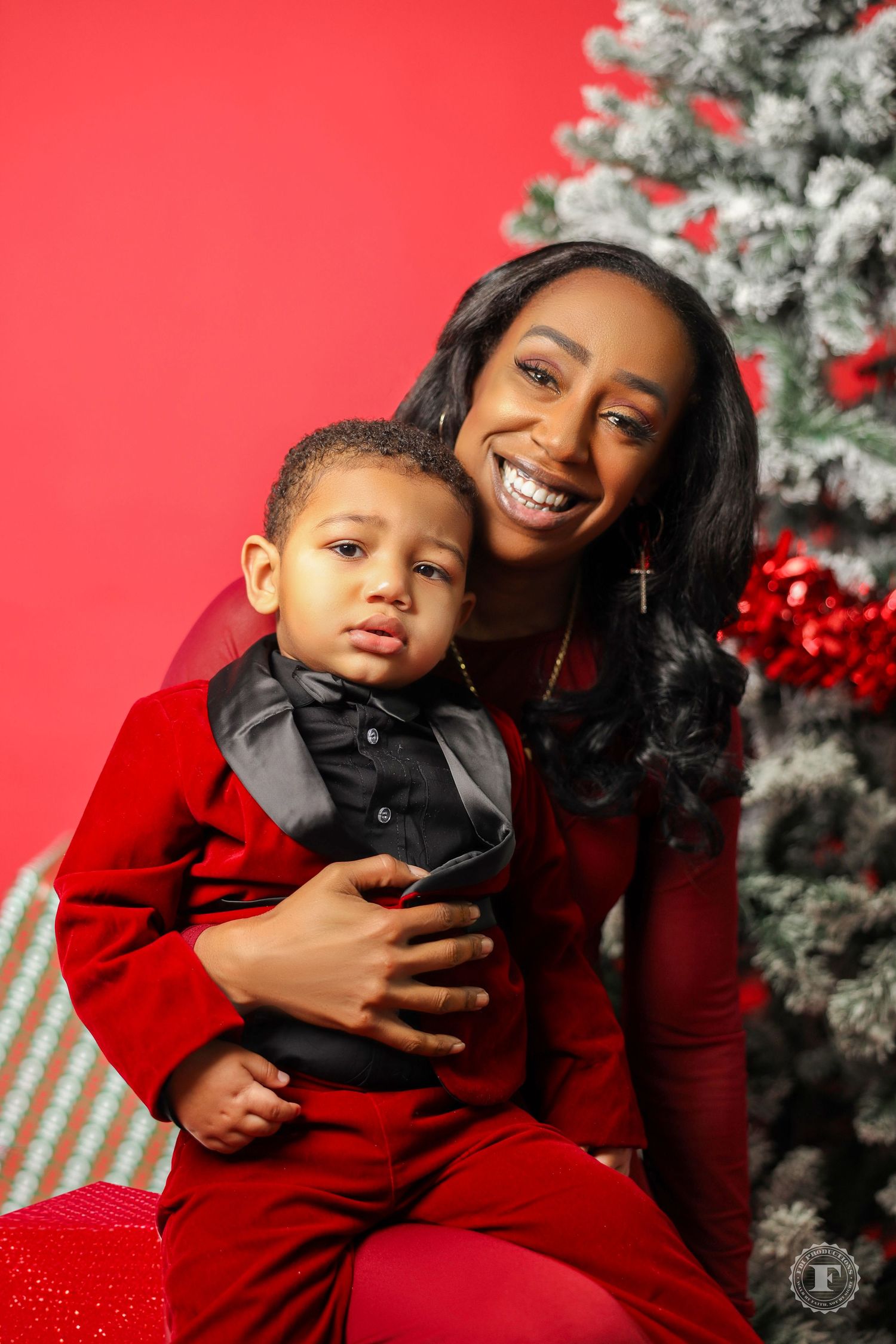 A festive holiday portrait with matching red outfits in front of a decorated Christmas tree against a bright red background.