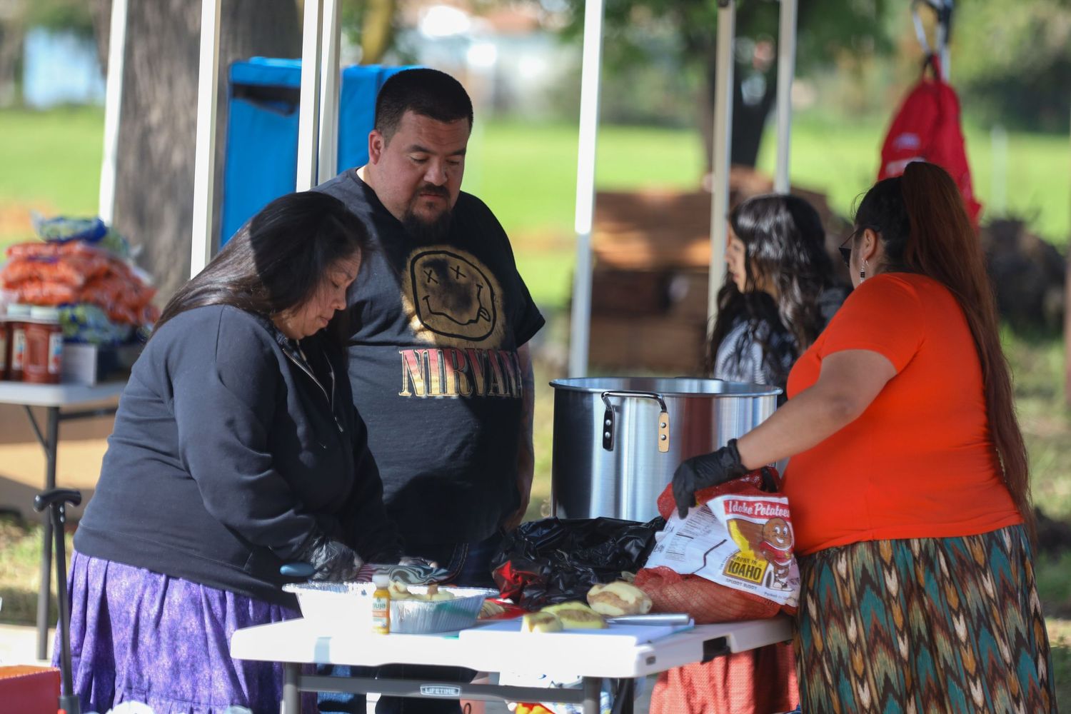 Group of people preparing food together at outdoor tables with cooking equipment at a community gathering.