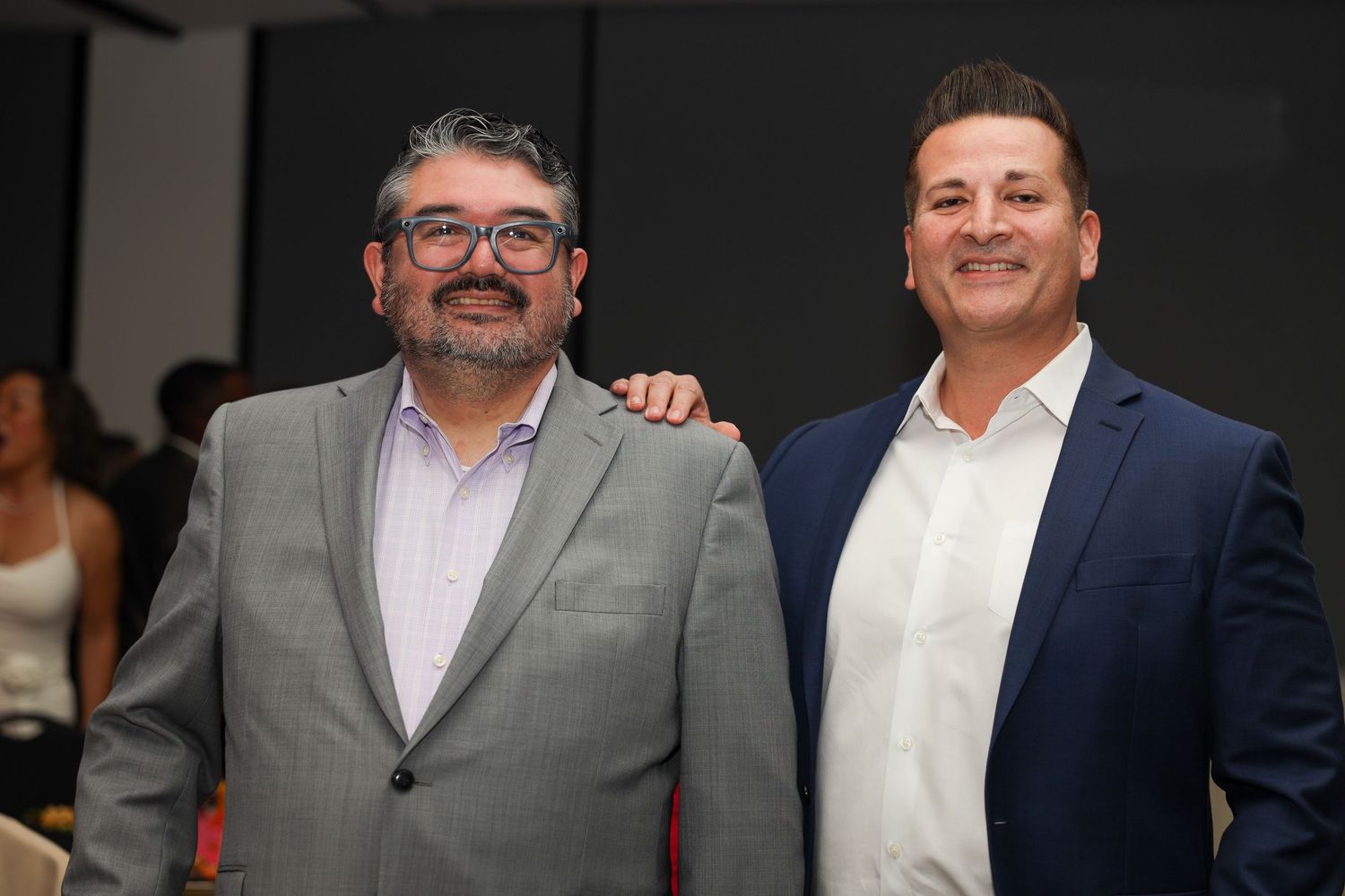 Two businessmen in suits stand together smiling at a professional event.