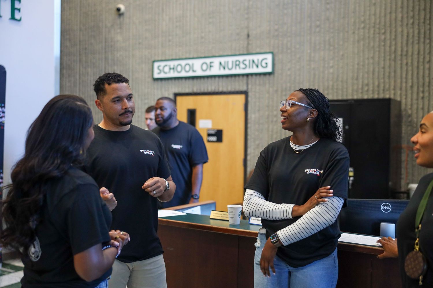 Students and faculty gather for a social event in a nursing school hallway with refreshments.