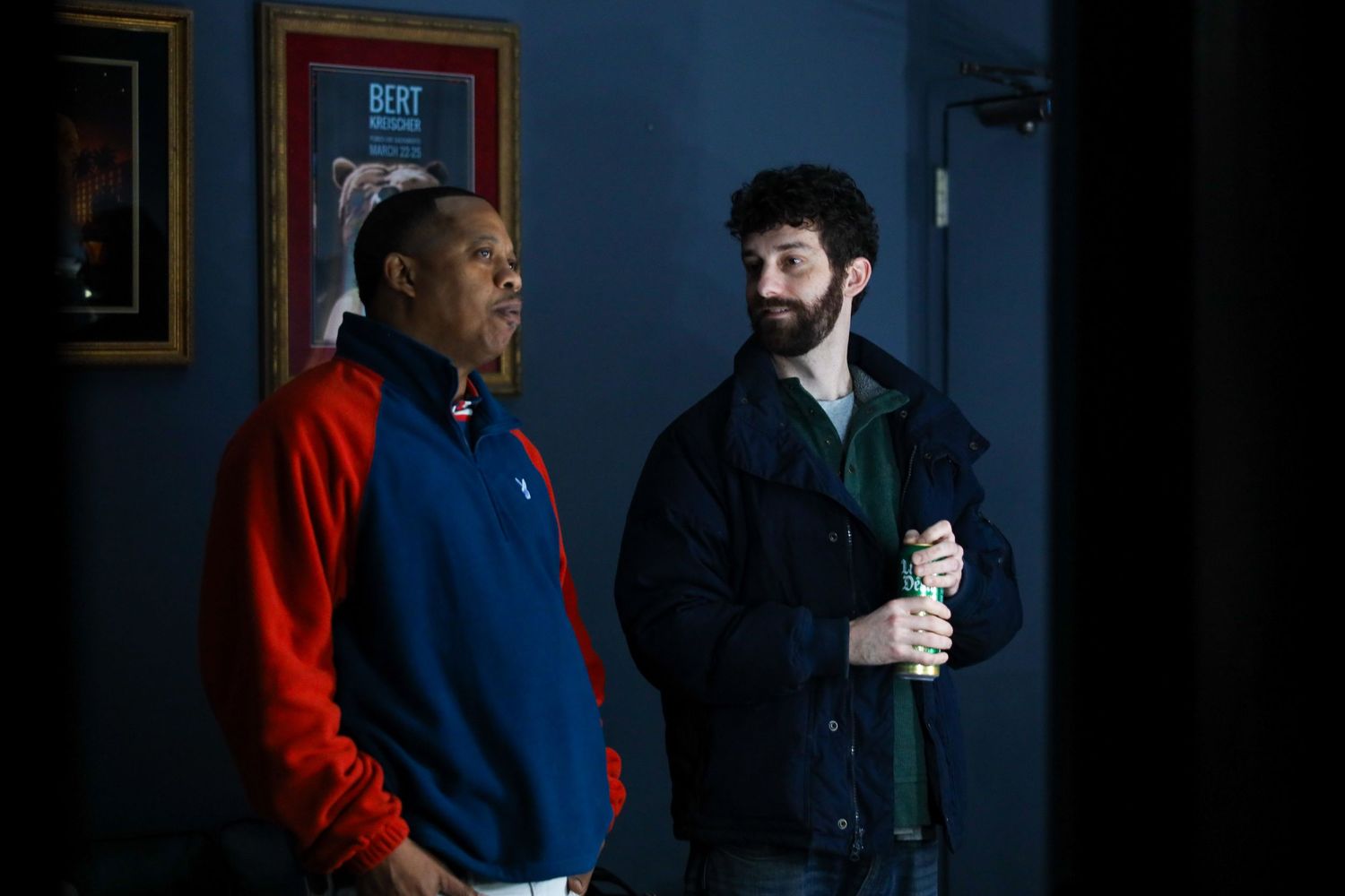 Three people stand in conversation at an indoor event with dark lighting and blue tones.
