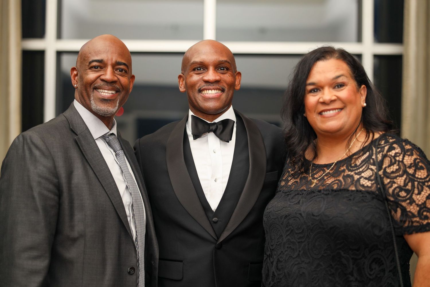 A group of formally dressed people in black tie attire pose together at an elegant event.