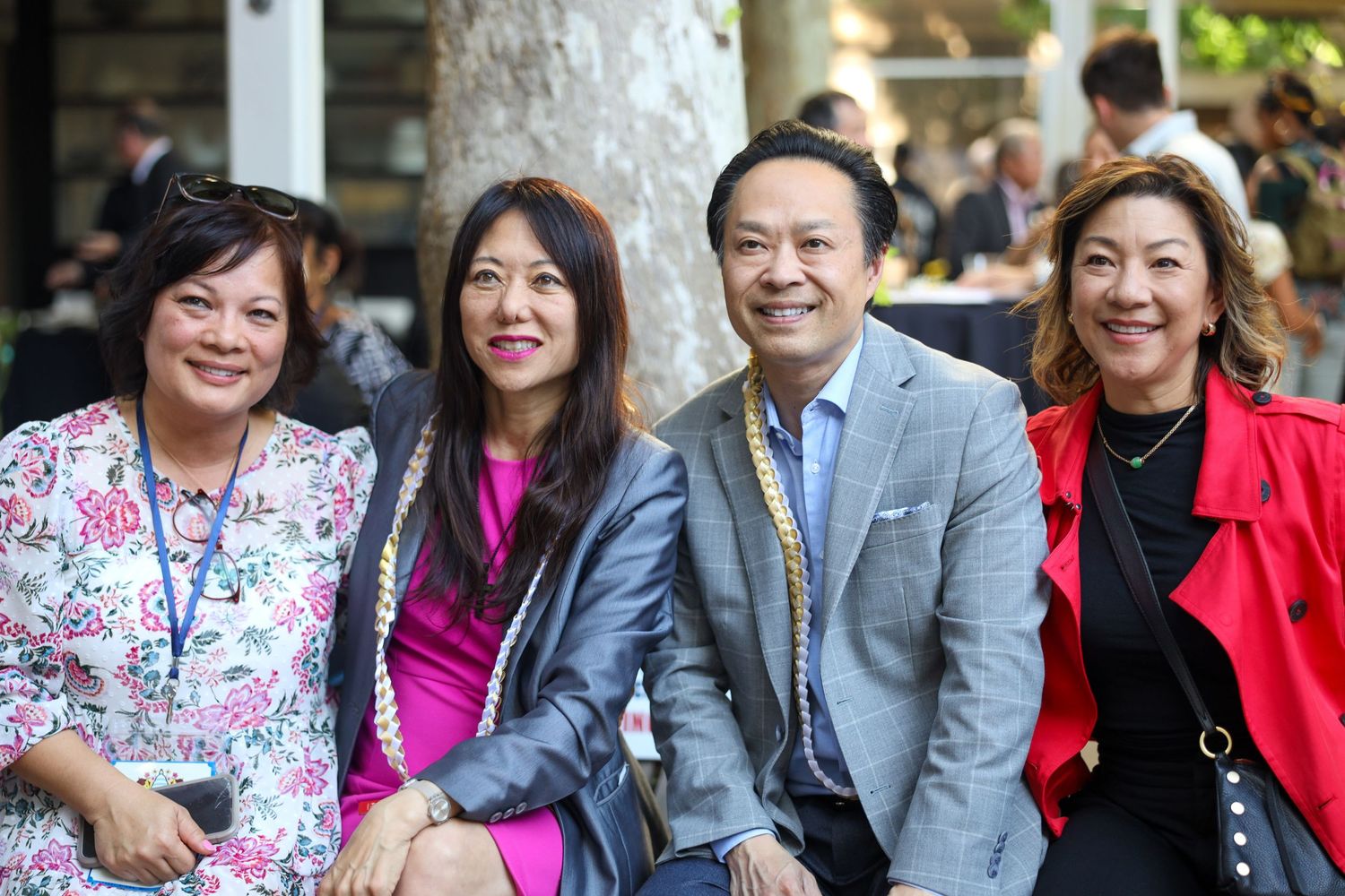 Four smiling Asian professionals posing together outdoors at a social event, dressed in colorful business attire.