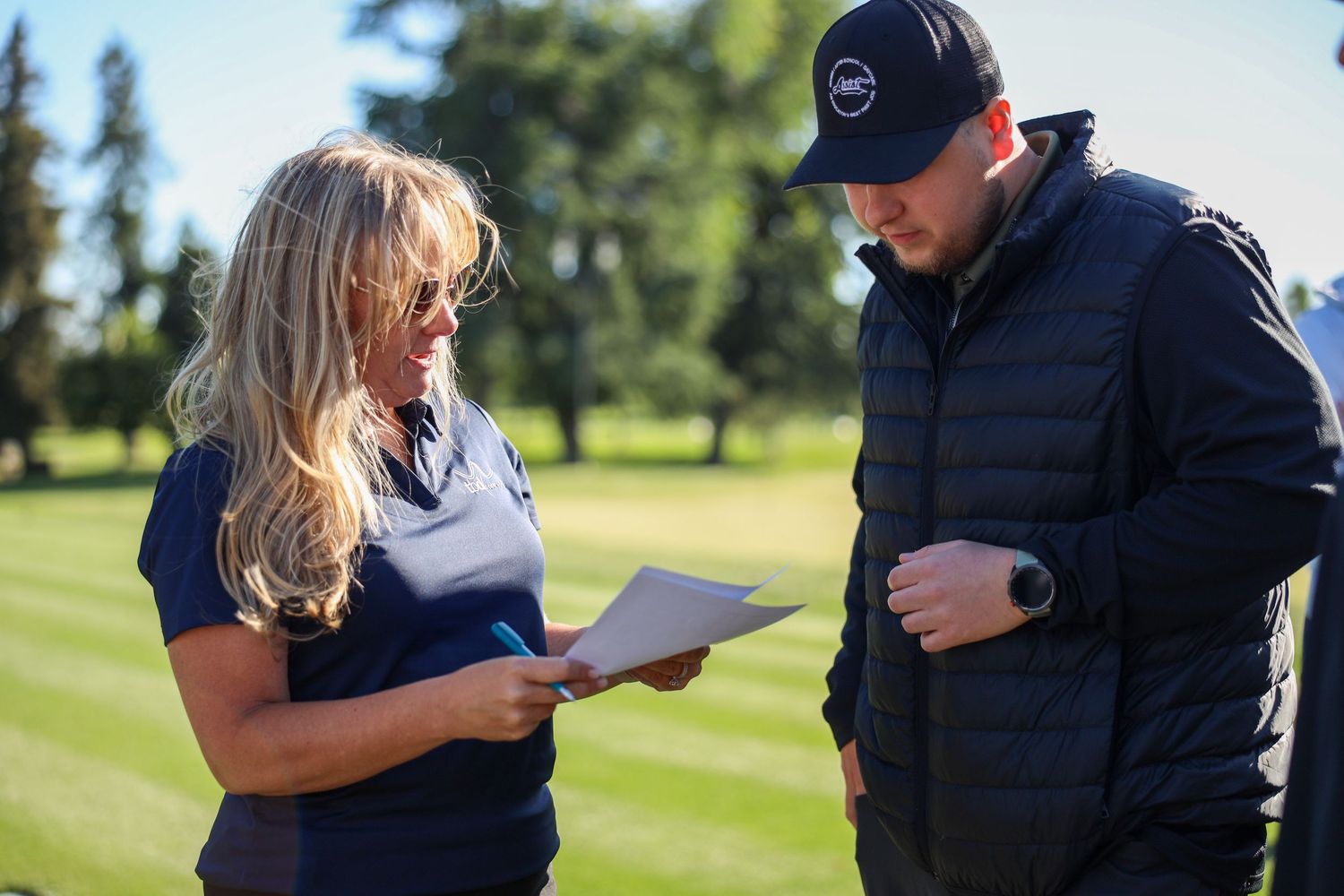 A woman and man reviewing documents together on a golf course on a sunny day.